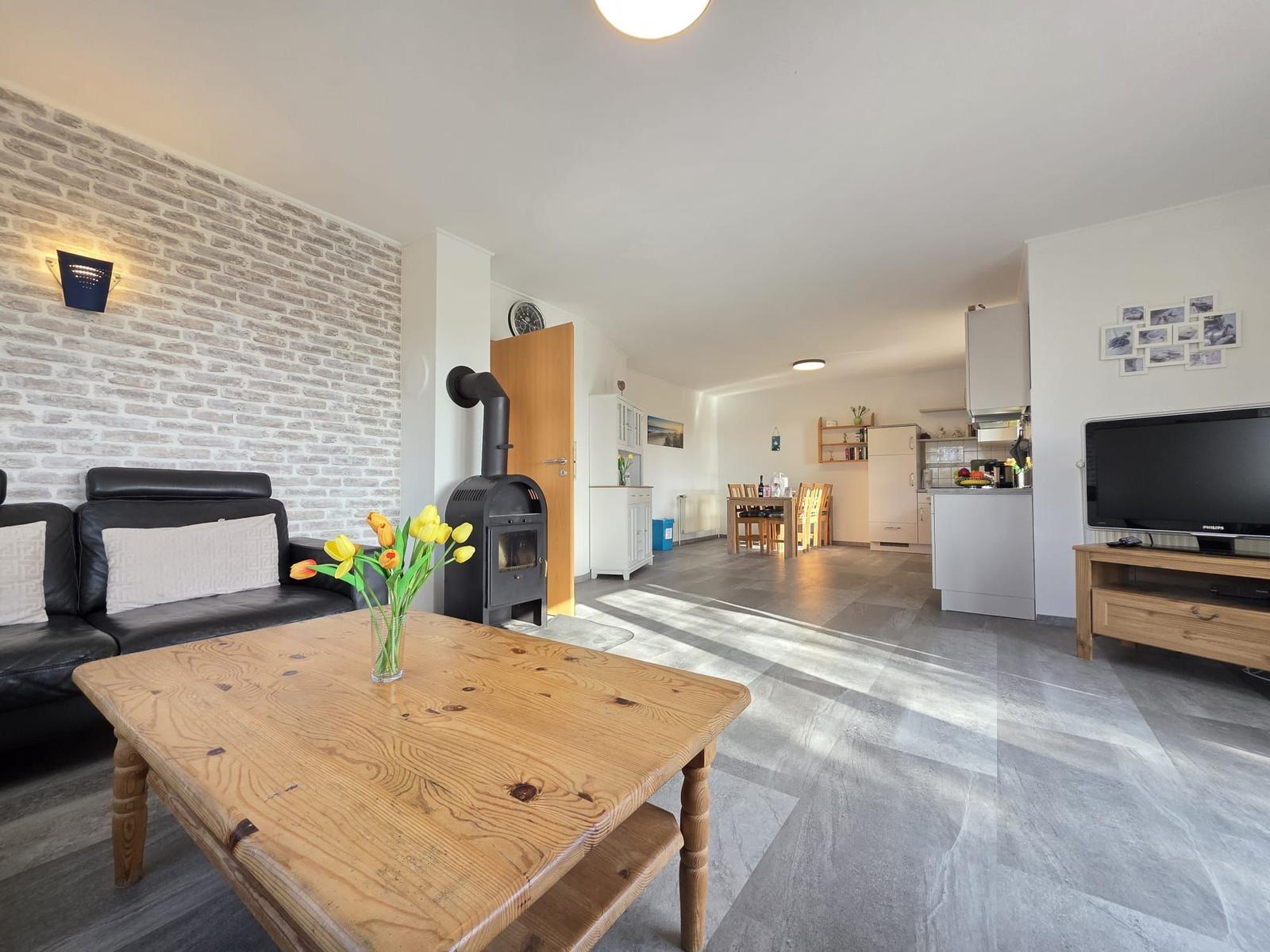 Wohn- und Essbereich mit Holztisch, Sofa und Kaminofen. Küche im Hintergrund.