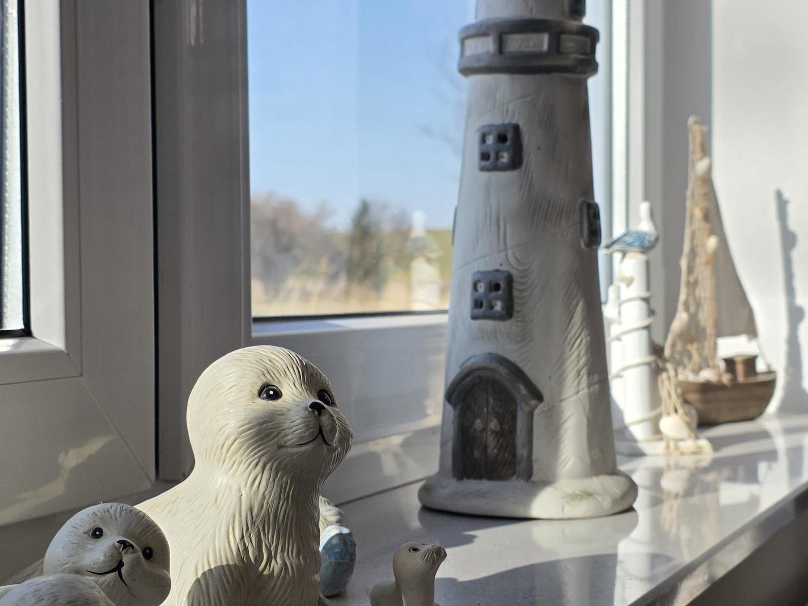 Seehundfiguren und Leuchtturm auf Fensterbank mit Blick nach draußen.