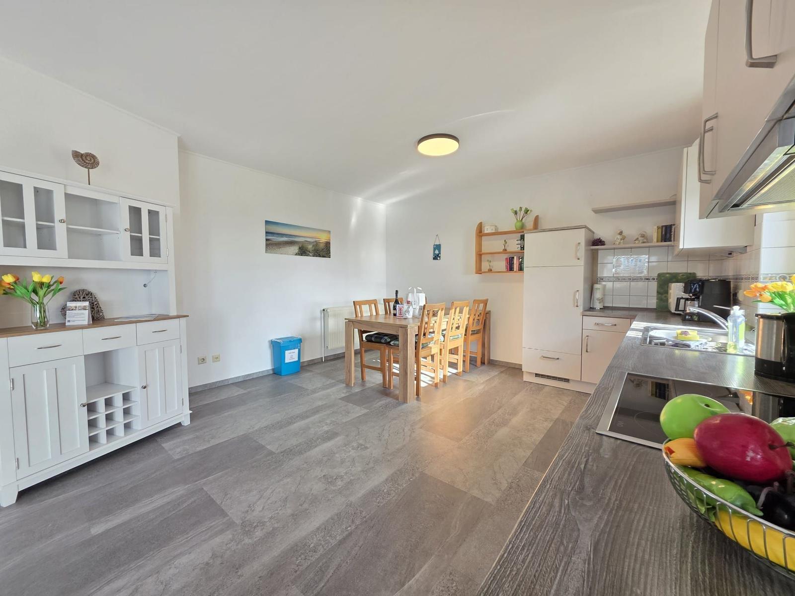 Küche und Essbereich mit Holztisch, weißen Schränken und grauem Boden.