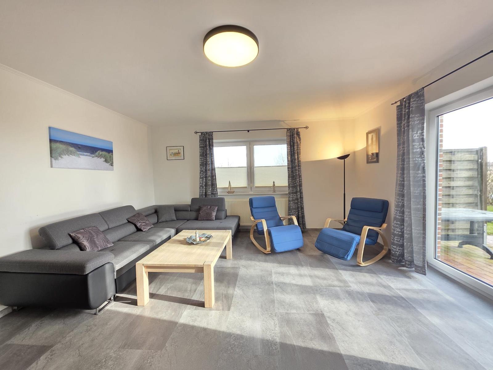 Wohnzimmer mit grauem Sofa, zwei blauen Sesseln und Holztisch.