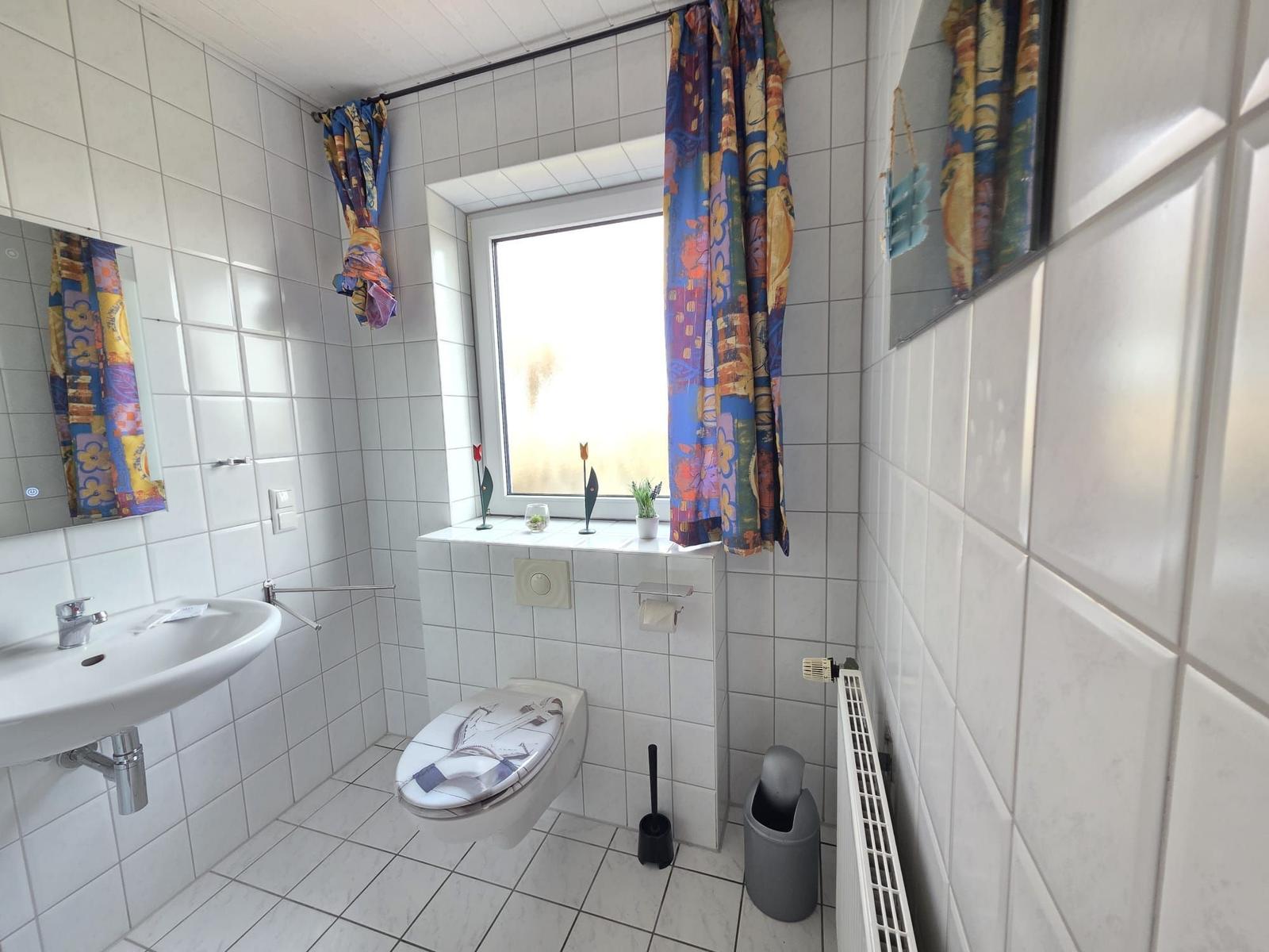 Badezimmer mit Toilette, Waschbecken und Fenster mit bunten Vorhängen.