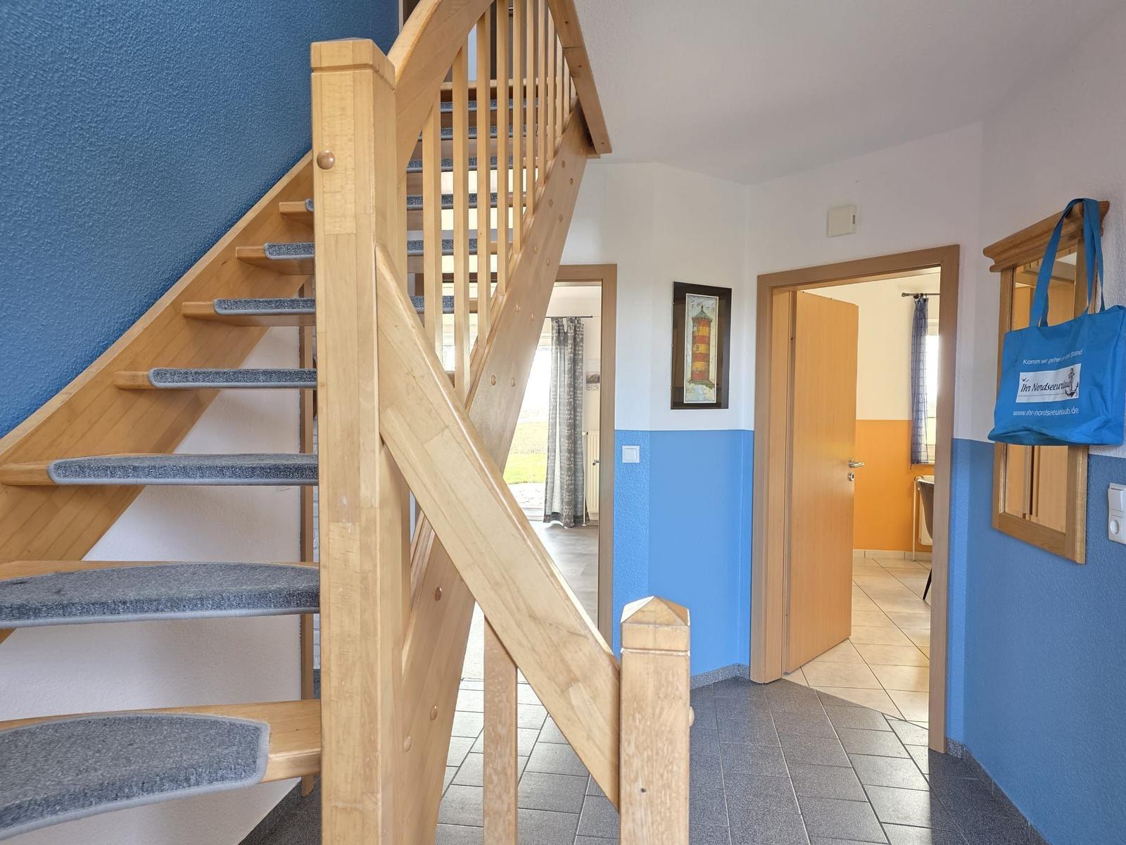 Holztreppenhaus mit blauen Wänden und Blick in Wohn- und Schlafzimmer.