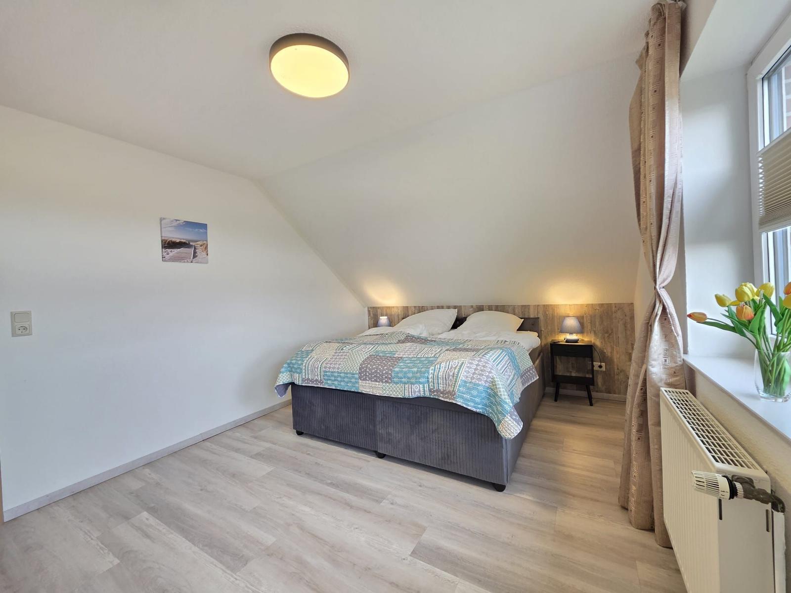 Schlafzimmer mit Doppelbett, Holzfußboden und Fenster mit Blumen.