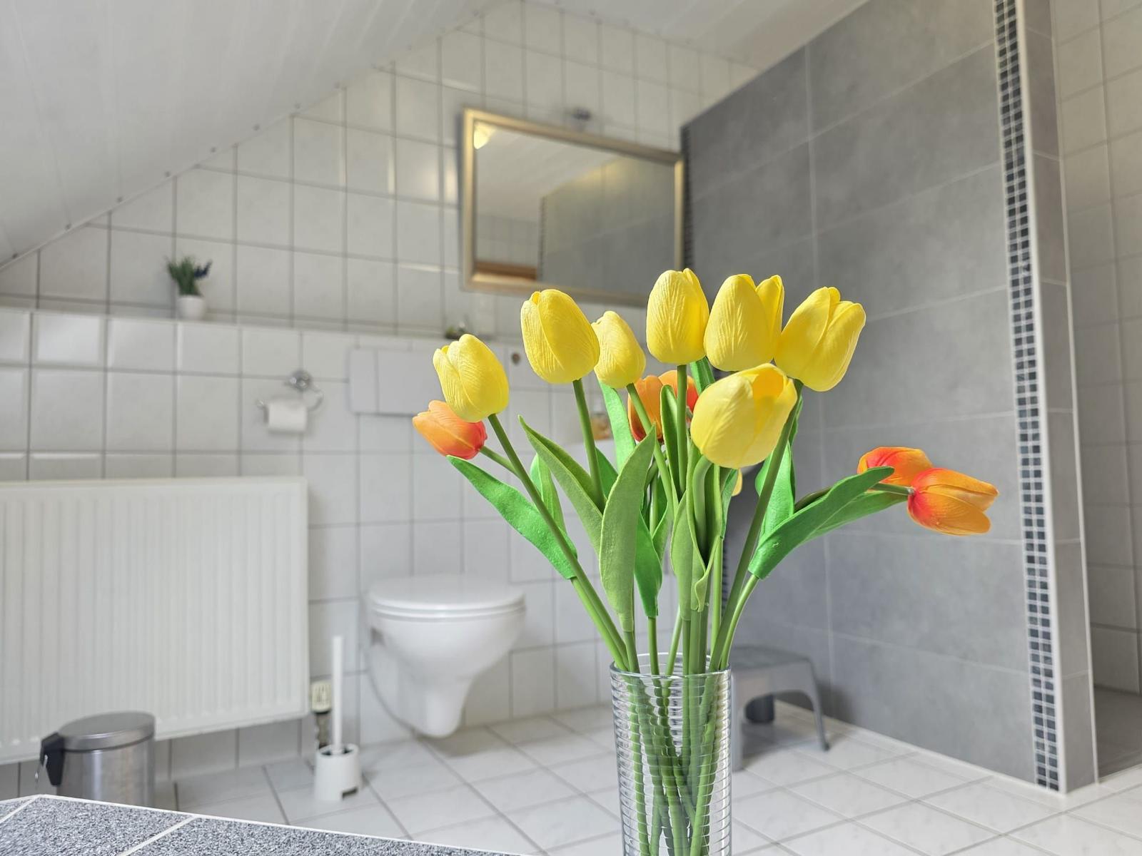 Bad mit Tulpen in Glas, Toilette, Spiegel und Dusche.