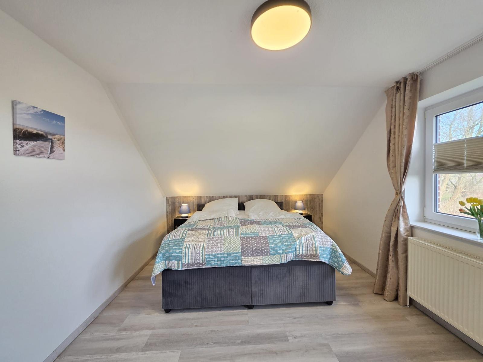 Schlafzimmer mit Doppelbett, Holzboden und Fenster mit Vorhängen.