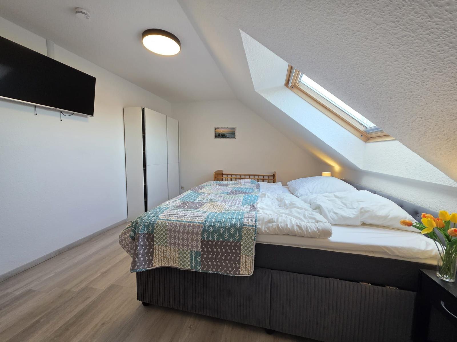 Schlafzimmer mit Dachschrägen, Bett, TV und Dachfenster.
