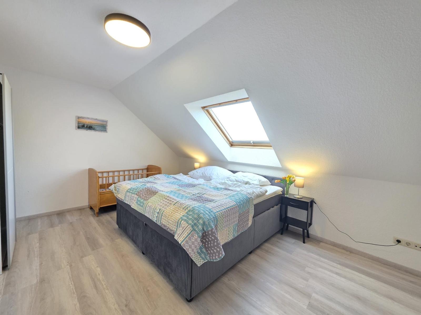 Schlafzimmer mit Dachschrägen, Dachfenster, Bett, Nachttisch und Kinderbett.