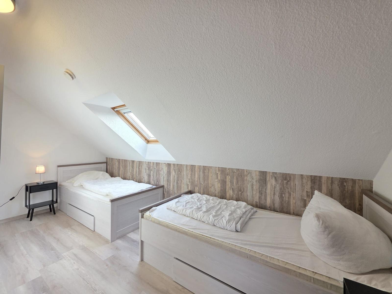Zwei Einzelbetten in einem Dachzimmer mit Holzverkleidung und Dachfenster.