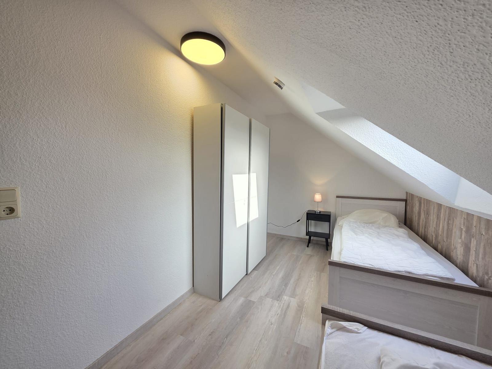 Zimmer mit Dachschrägen, Bett, Kleiderschrank und Nachttisch.