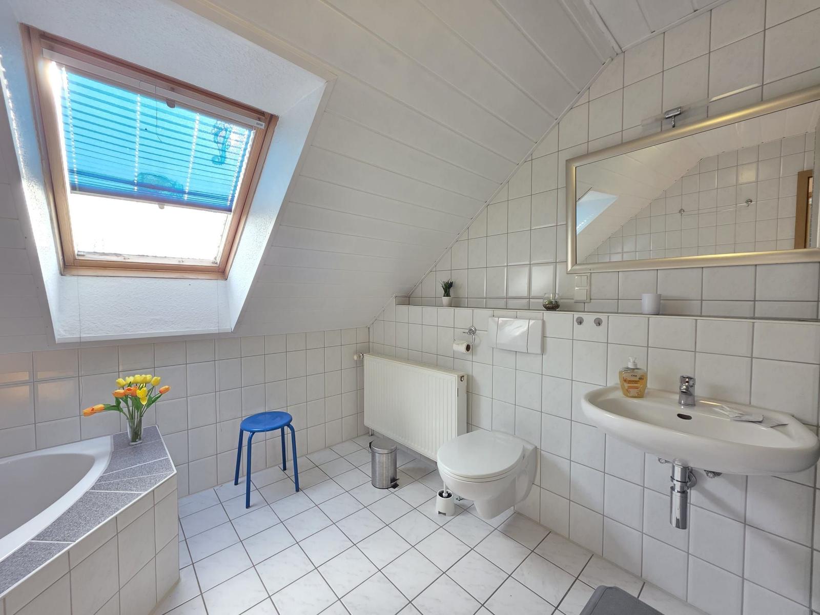 Badezimmer mit Dachschrägen, Fenster, Waschbecken, Toilette und Badewanne.