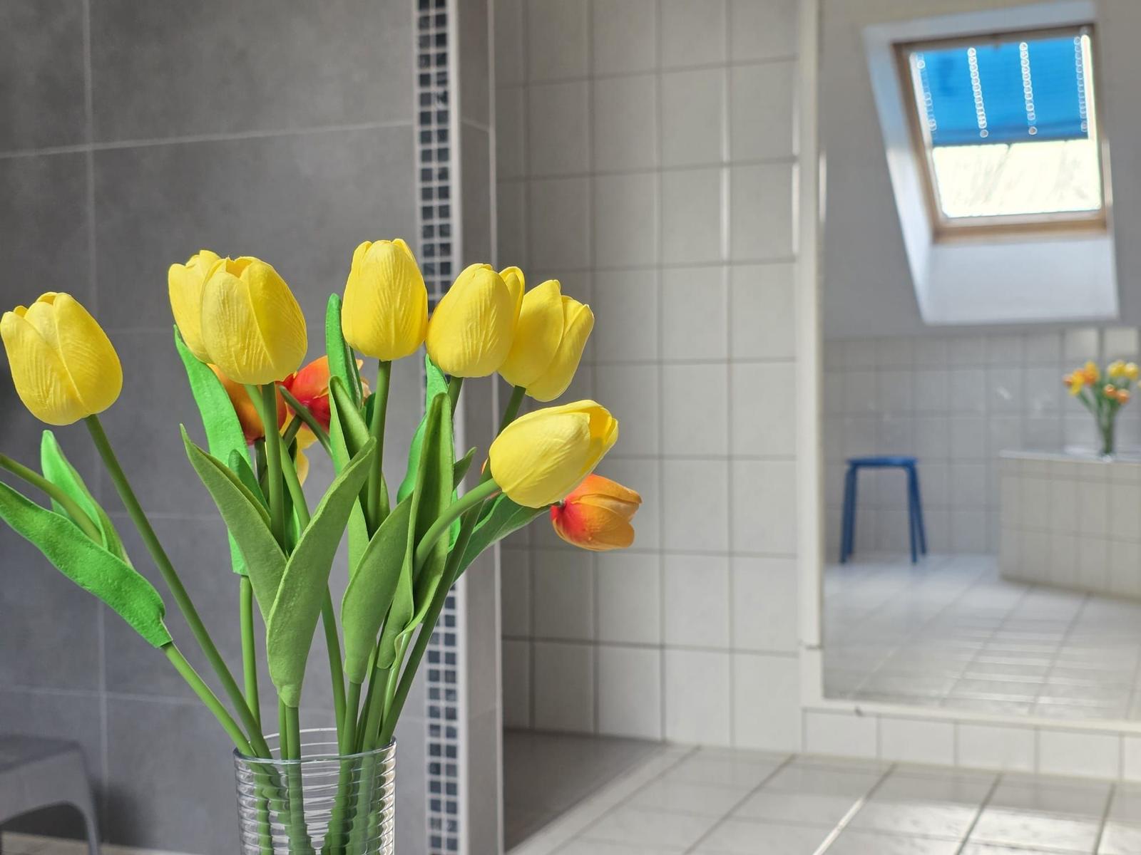 Badezimmer mit gelben Tulpen in Vase und Dachfenster.