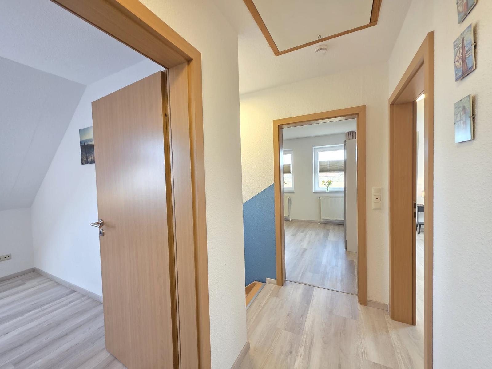 Flur mit Holztüren und hellen Wänden. Blick in Wohn- und Schlafzimmer.