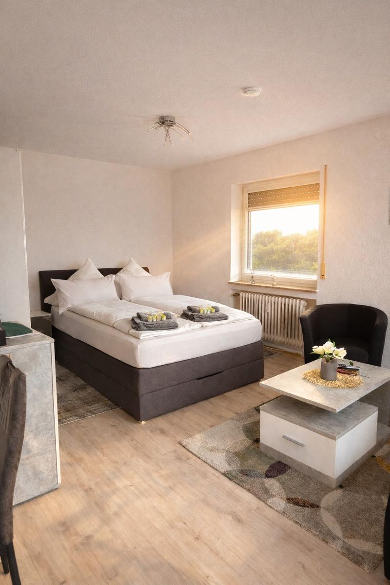 Schlafzimmer mit Doppelbett, Sitzgelegenheit und Fenster mit Blick auf Grün.