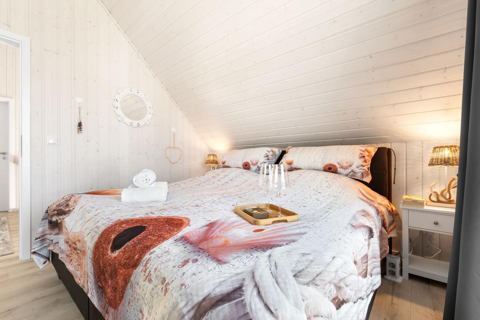 Schlafzimmer mit Bett, Nachttisch und Lampe. Decke mit Muster. Holzwände und Dachschräge.