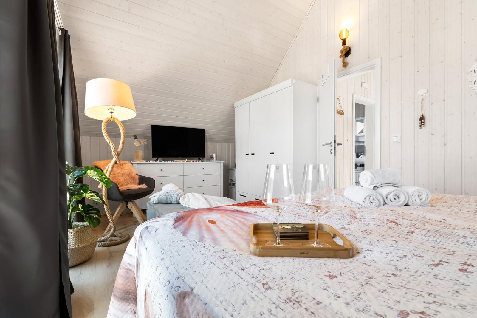 Schlafzimmer mit Bett, Kleiderschrank und Fernseher. Auf dem Bett stehen Gläser und Handtücher.