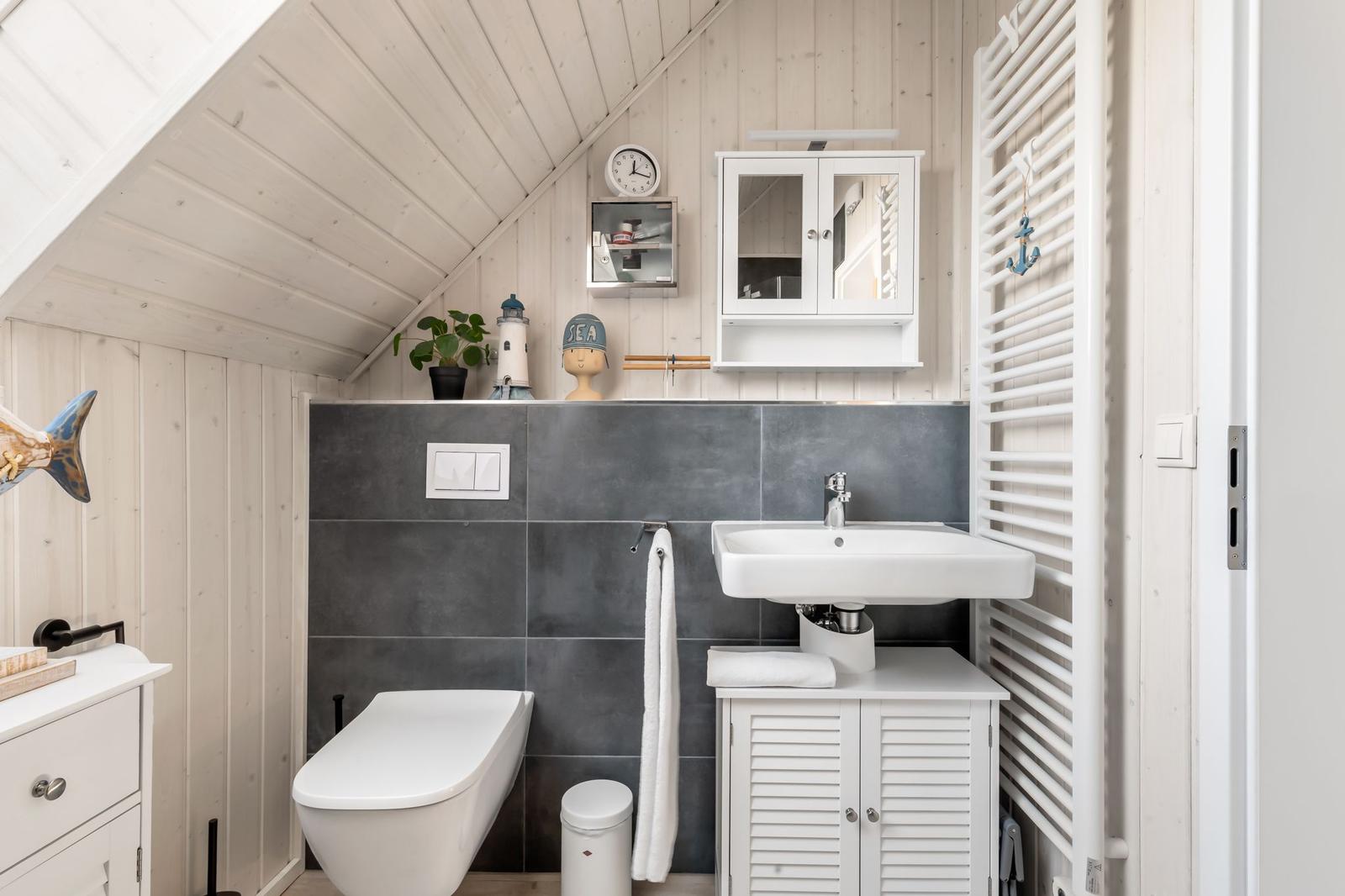 Badezimmer mit Toilette, Waschbecken und Heizkörper. Holzwände und graue Fliesen.