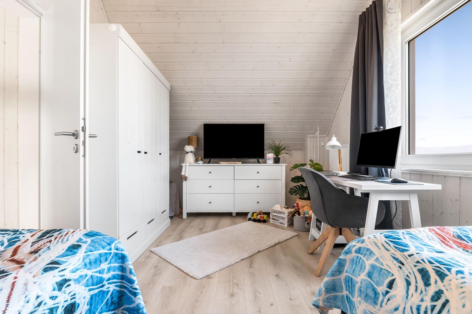Zimmer mit zwei Betten, Schreibtisch, TV und Kleiderschrank. Holzboden und großes Fenster.