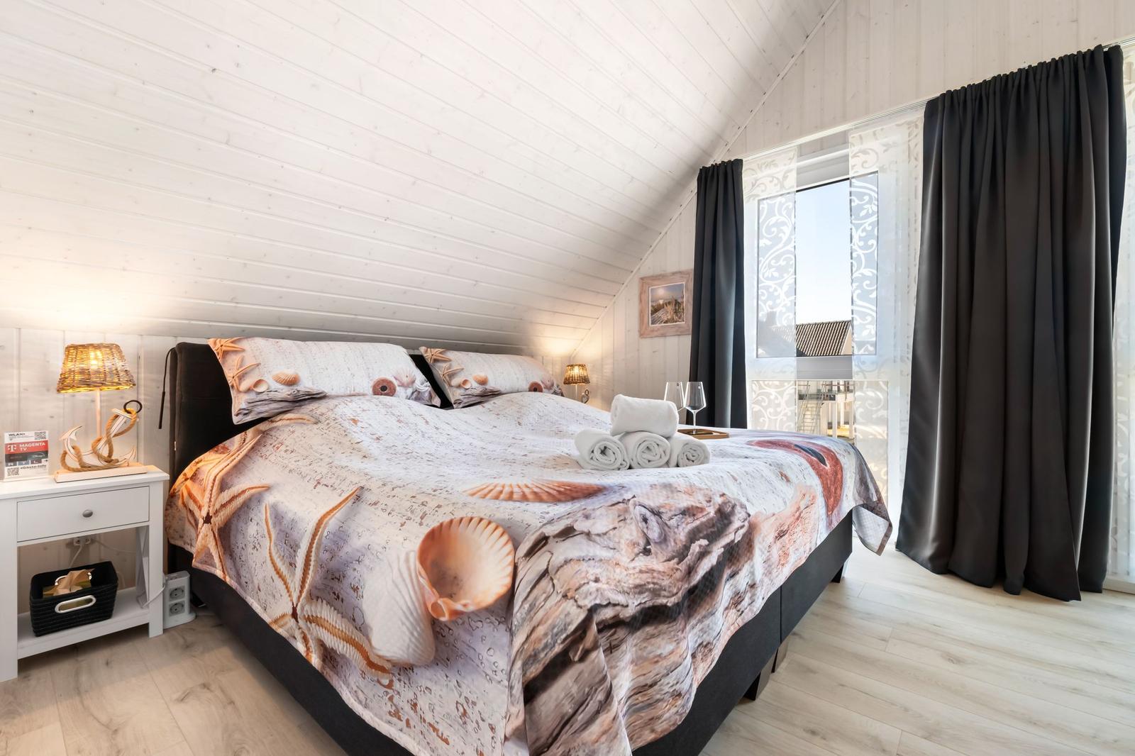 Schlafzimmer mit Bett, Nachttisch und Fenster mit Vorhängen.