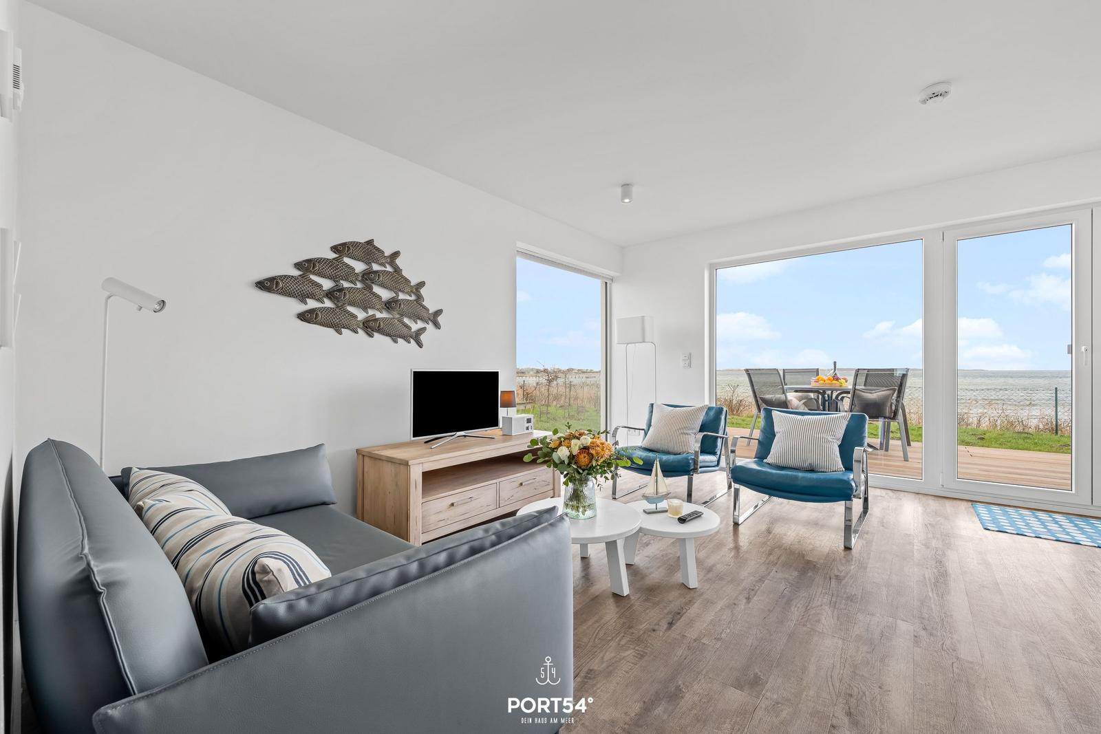 Wohnzimmer mit Sofa, Fernseher und Blick auf Terrasse und Meer.
