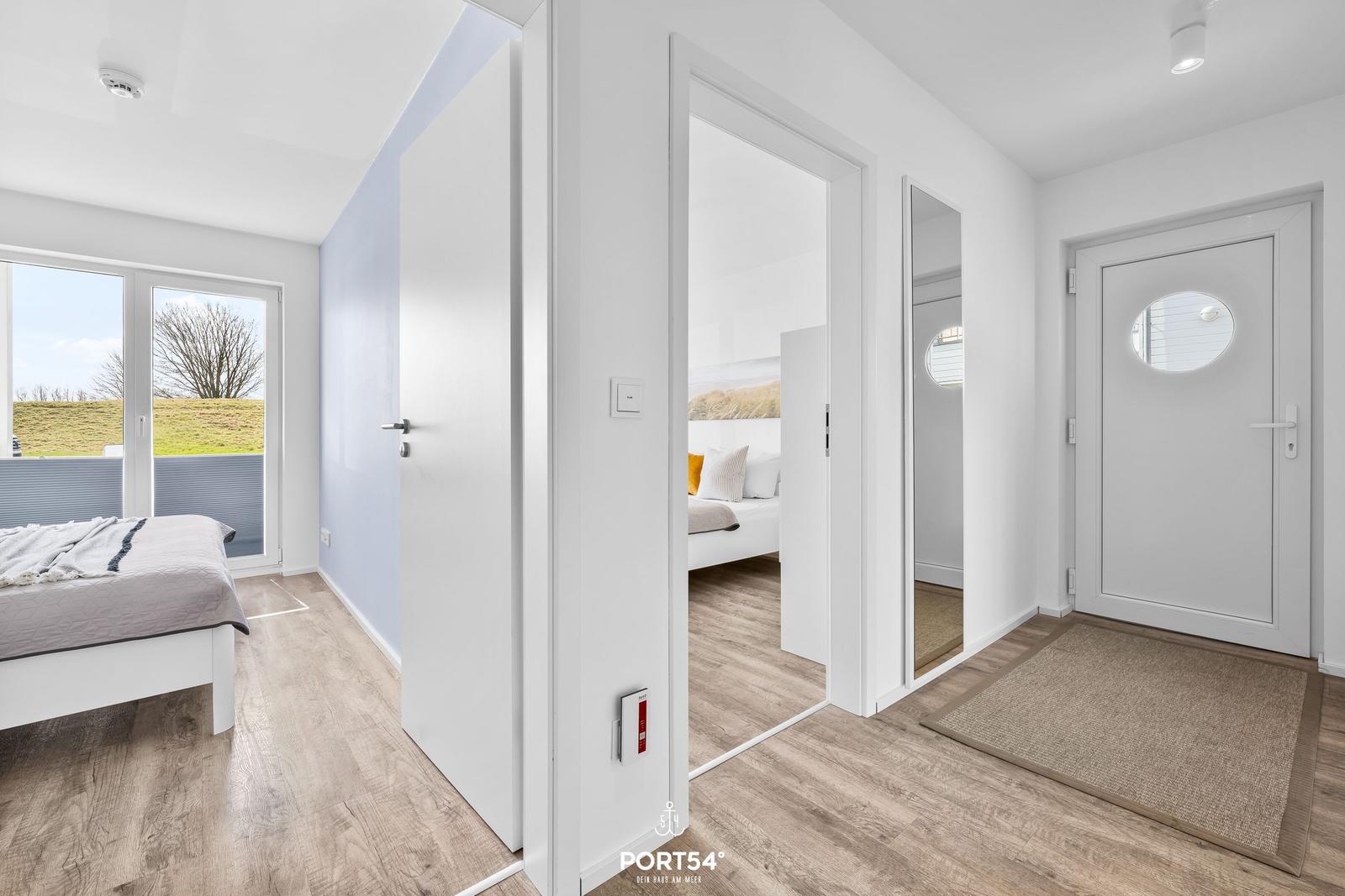 Schlafzimmer mit Blick auf Grünfläche, Flur mit Tür und Spiegel, Bodenbelag Holzoptik.