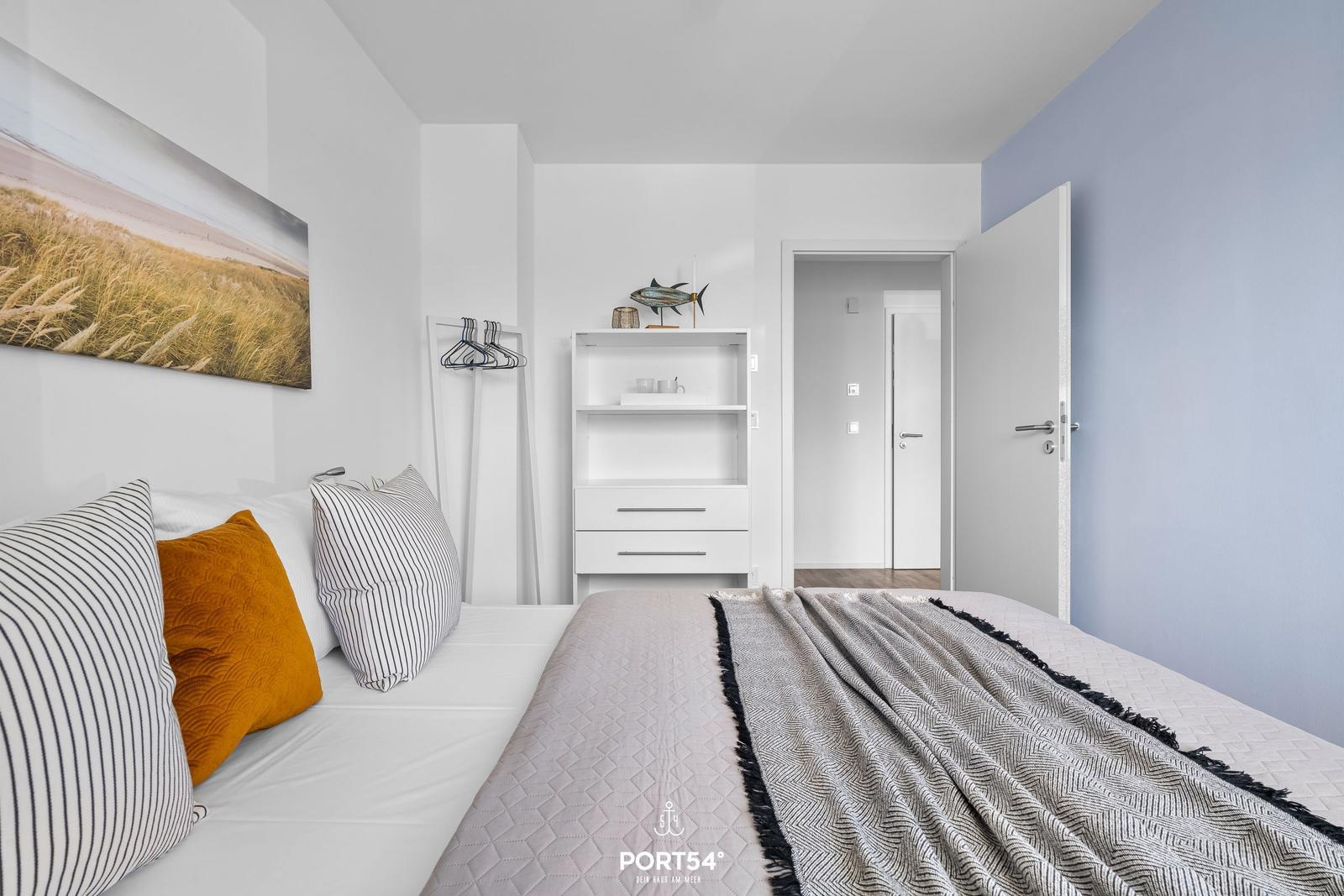 Schlafzimmer mit Bett, Wandbild und Schrank. Tür führt in angrenzenden Raum.