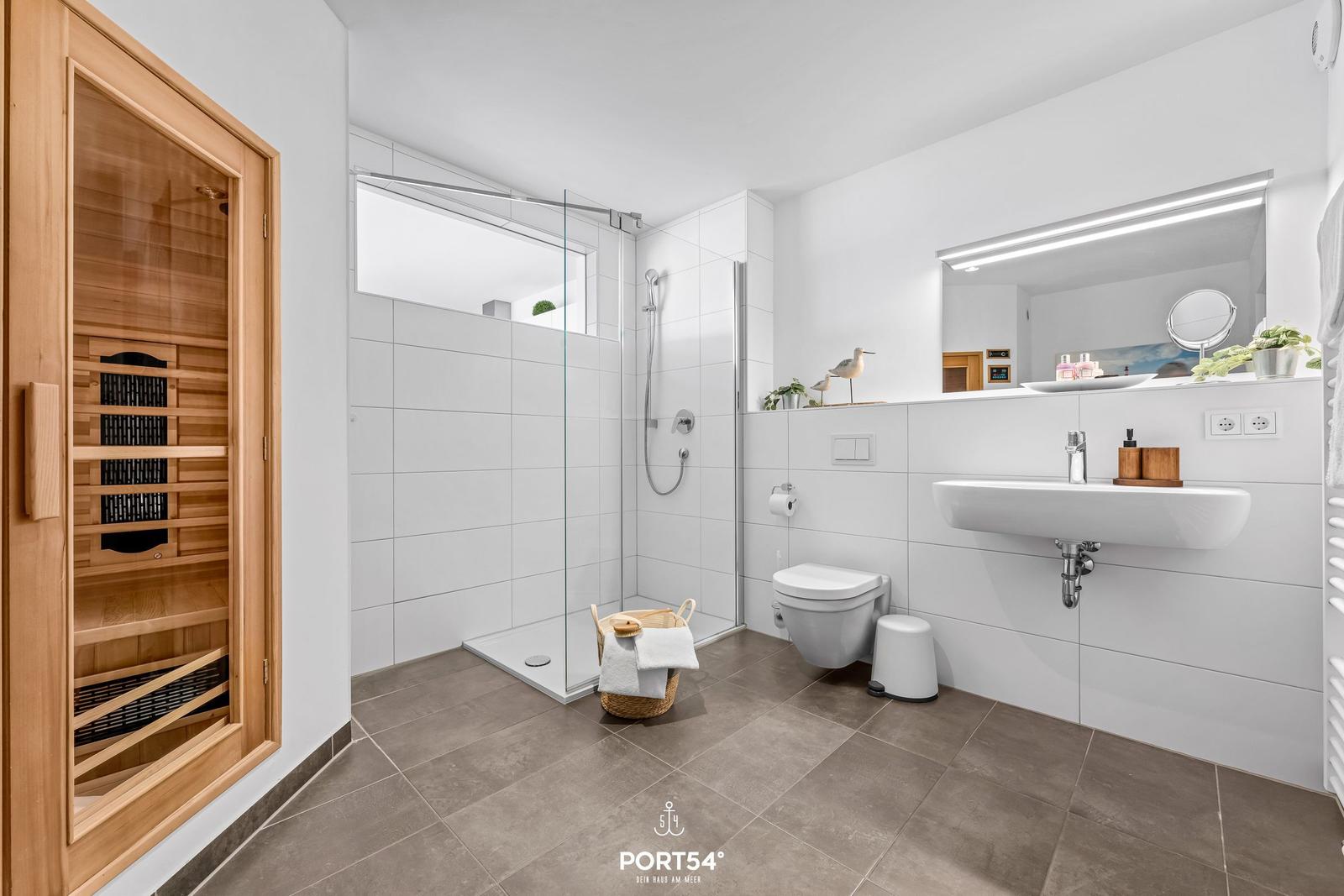 Bad mit Dusche, Toilette und Sauna. Weiße Fliesen, Holzrahmen und Spiegel.