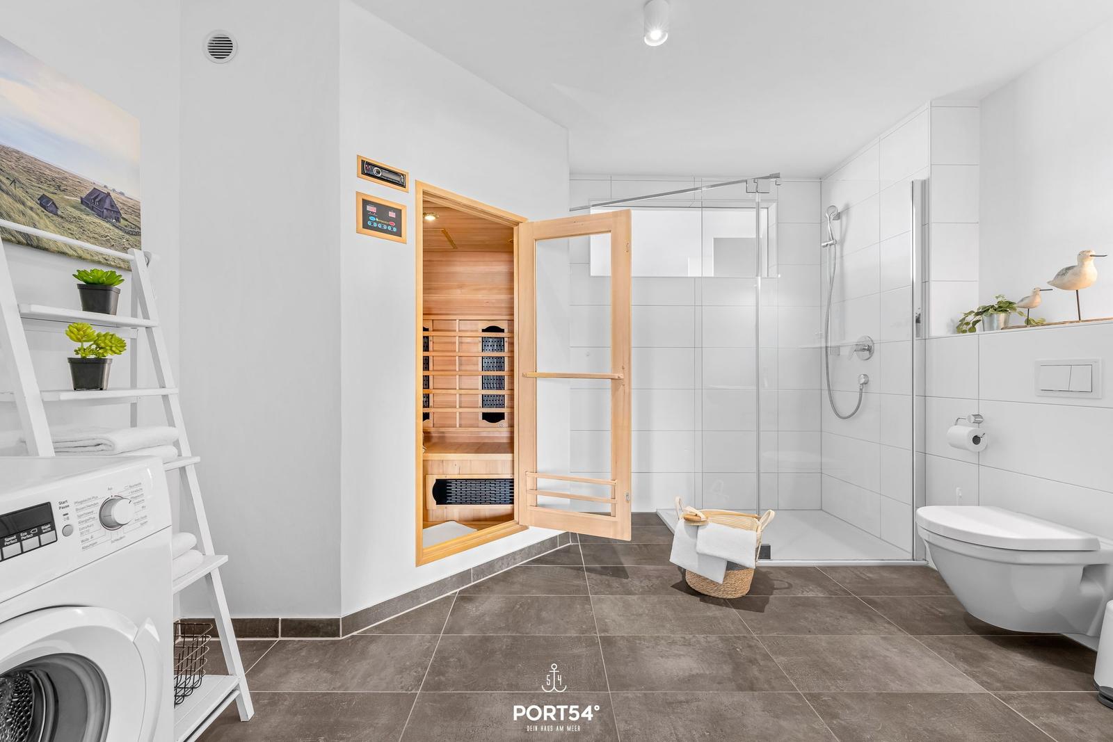Bad mit Sauna, Dusche und Waschmaschine. Weiße Wände, braune Fliesen.