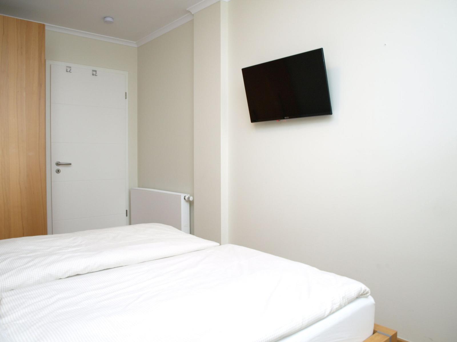 Ein Schlafzimmer mit Bett, Wandfernseher und Tür.