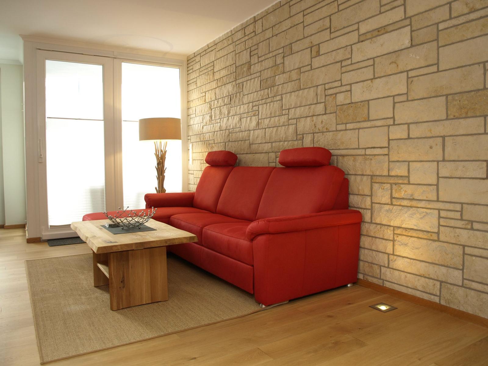 Ein roter Sofa mit Holztisch vor Steinwand und Fenster
