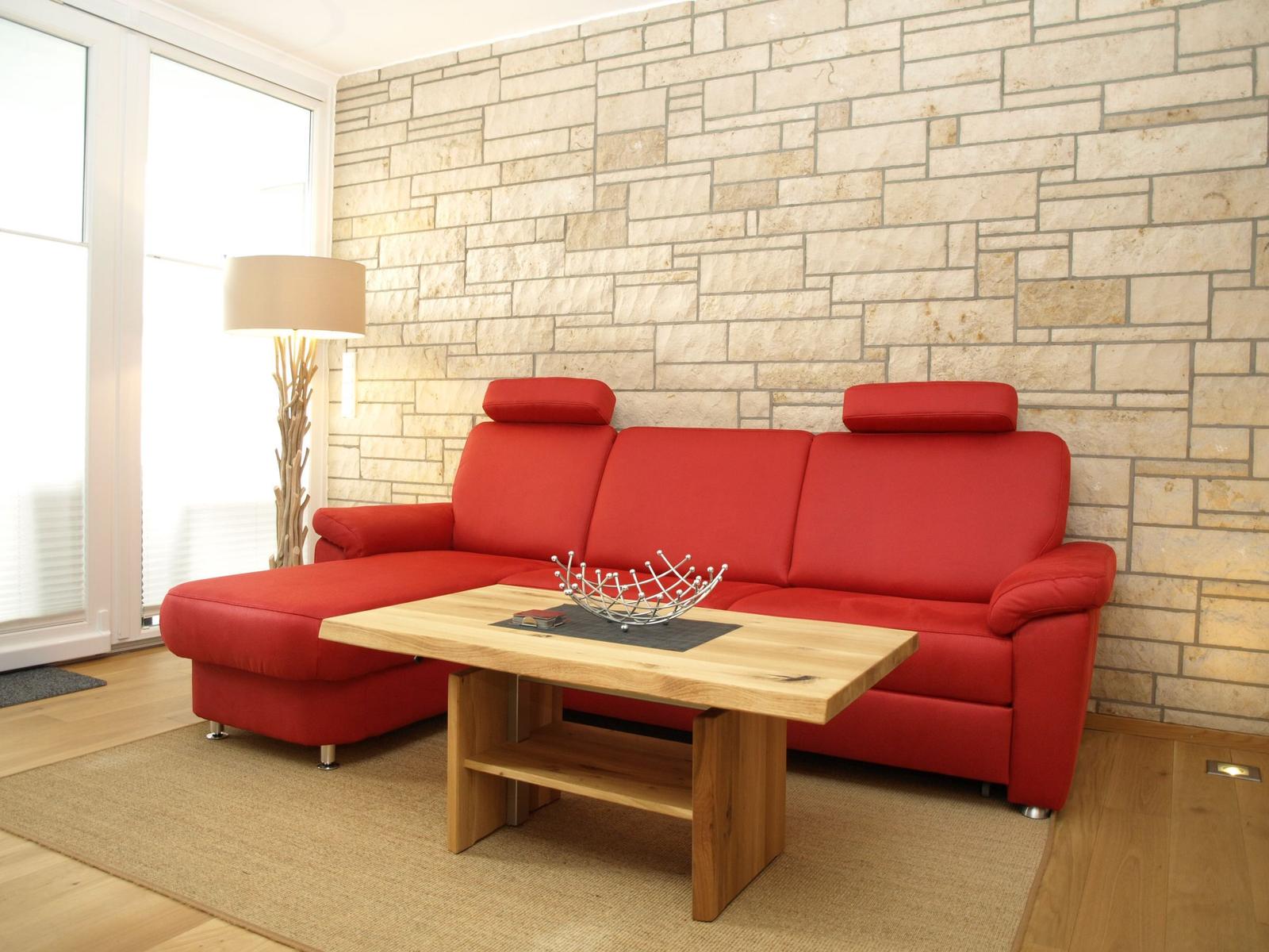 Ein rotes Sofa steht vor einer Steinwand. Davor befindet sich ein Holztisch.