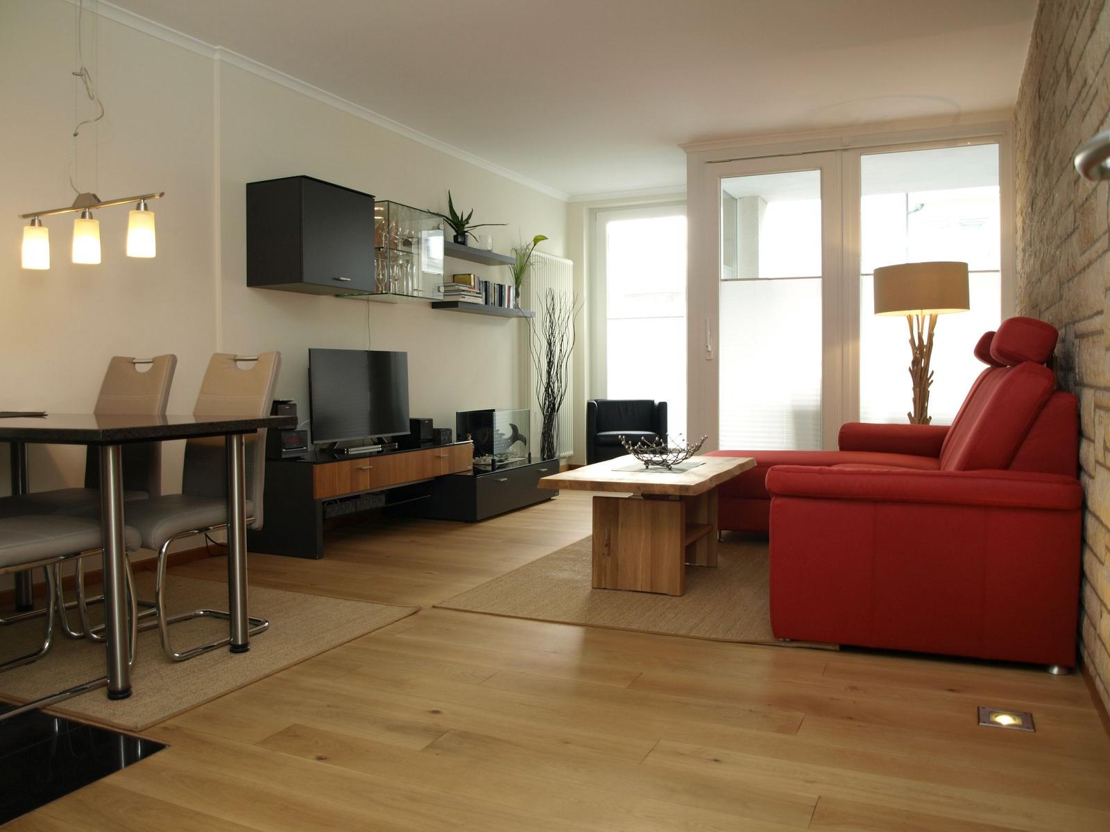 Wohn- und Essbereich mit rotem Sofa, Holzboden und TV-Möbeln.