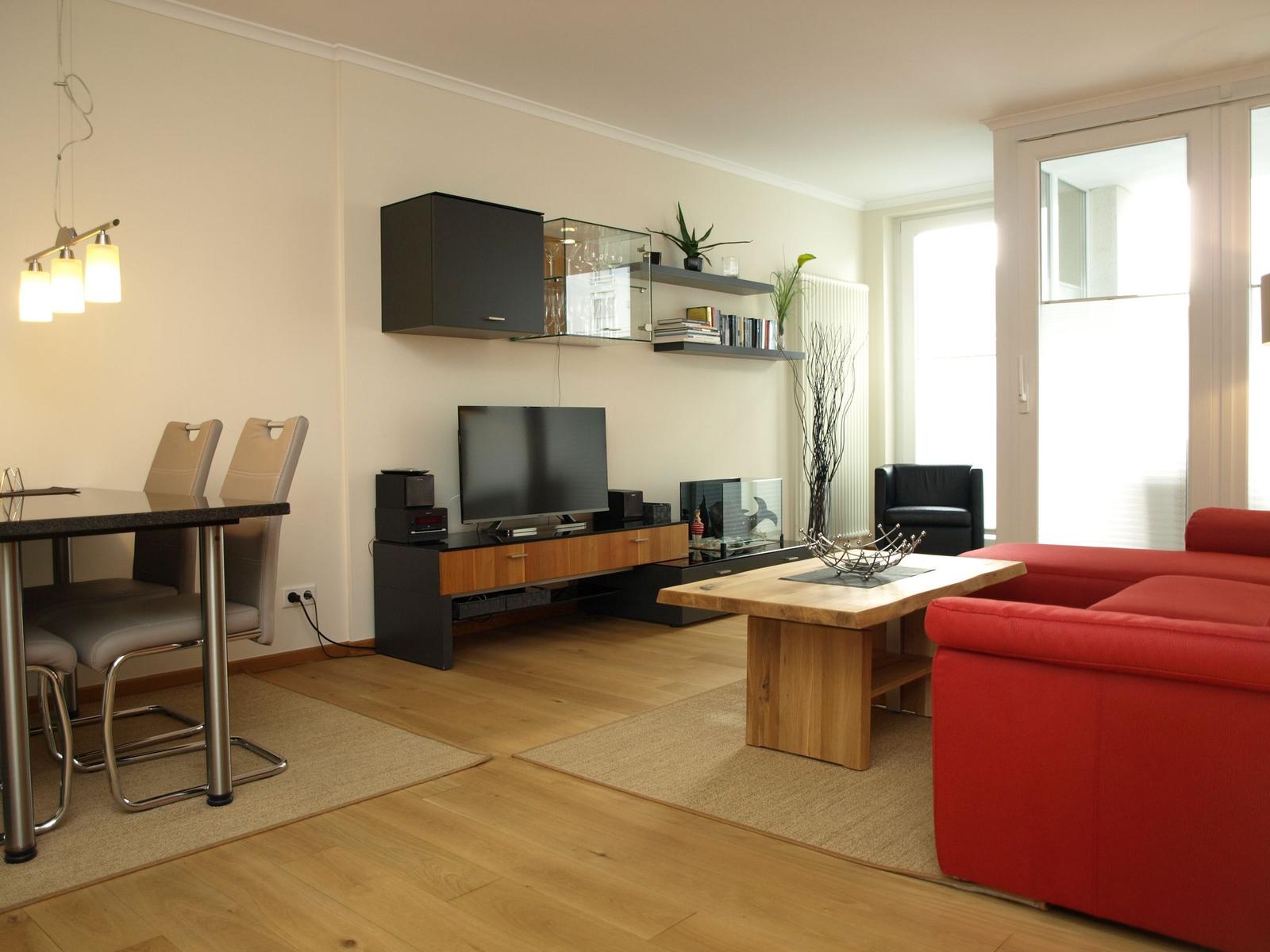Wohnzimmer mit rotem Sofa, Holztisch und TV-Möbel. Essbereich mit Tisch und Stühlen.