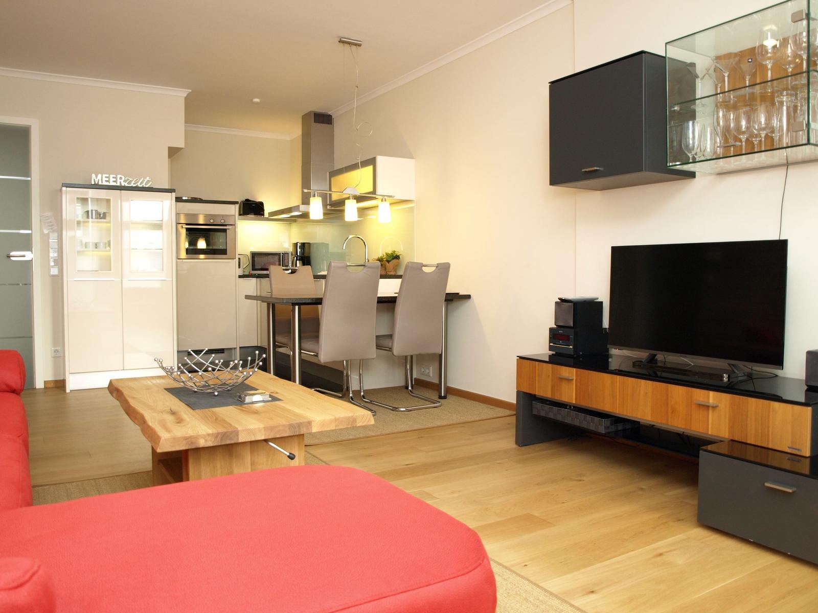 Wohnzimmer mit Küchenbereich, rotem Sofa und TV-Möbel