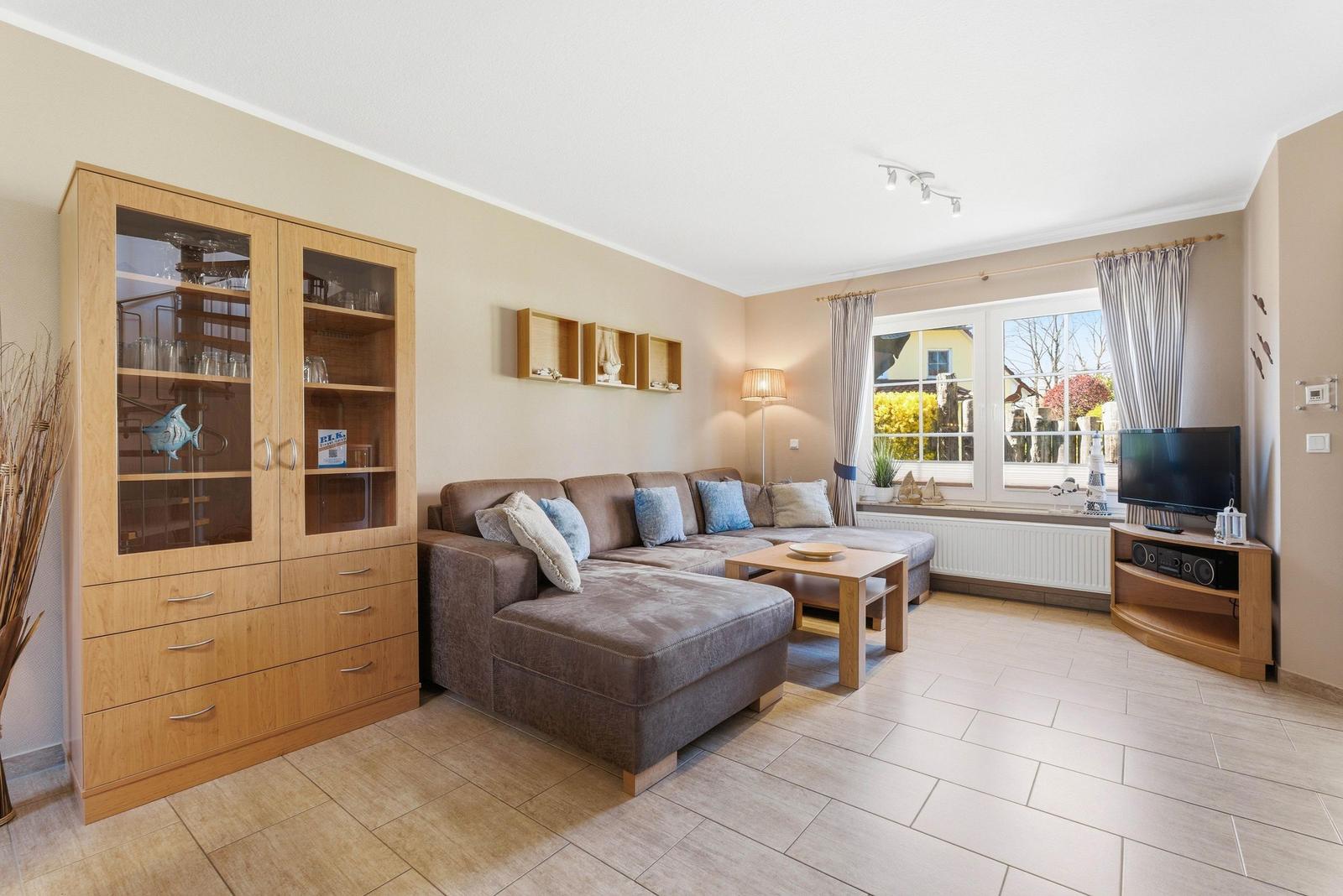 Wohnzimmer mit Sofa, TV und Glasvitrine. Fenster mit Blick nach draußen.
