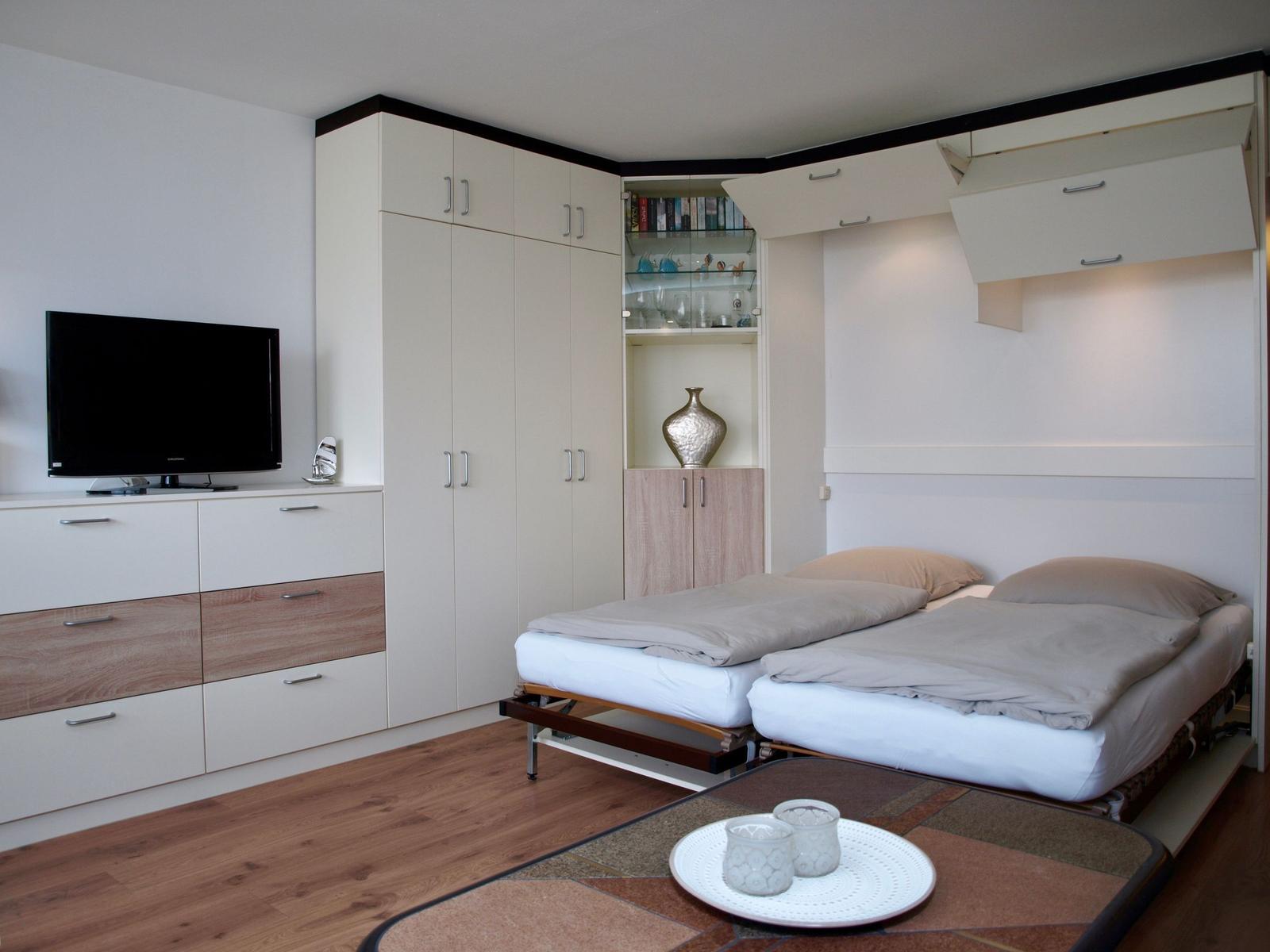 Zimmer mit Bett, Schränken und Fernseher. Holzfußboden und moderne Einrichtung.