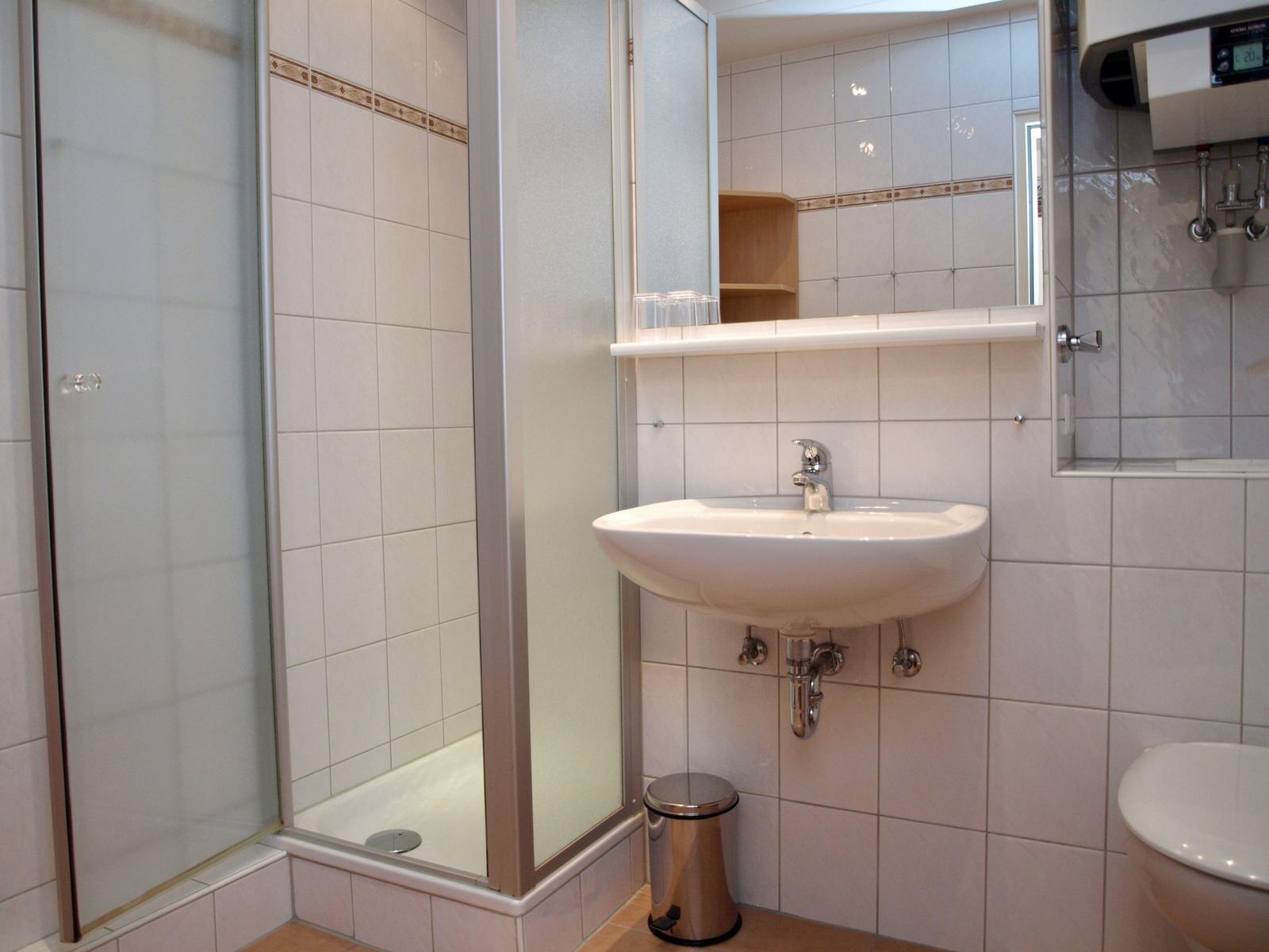 Badezimmer mit Dusche, Waschbecken und Toilette. Weiße Fliesen und Spiegelschrank.