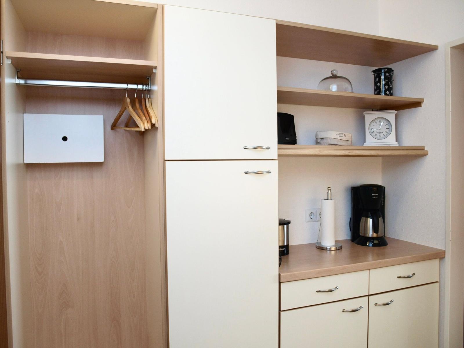 Kleiderkammer mit Kleiderständer und integrierte Küchenzeile mit Kaffeemaschine.