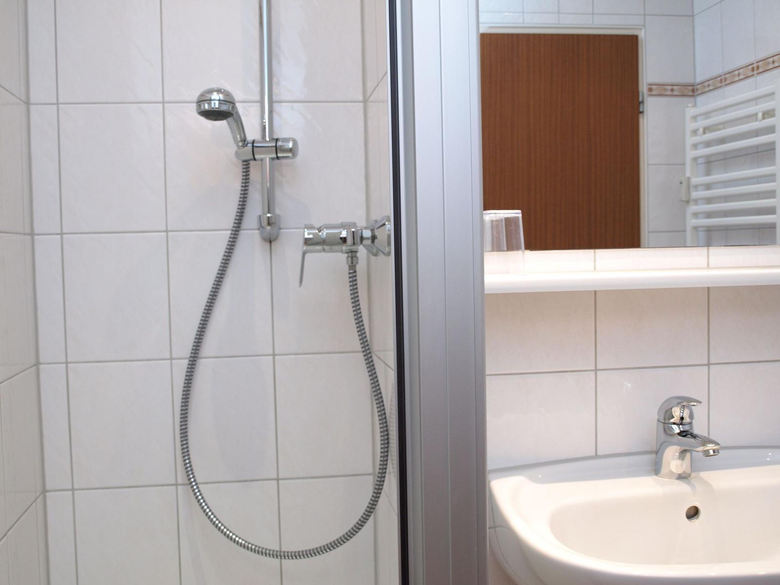 Dusche mit Handbrause und Waschbecken mit Wasserhahn