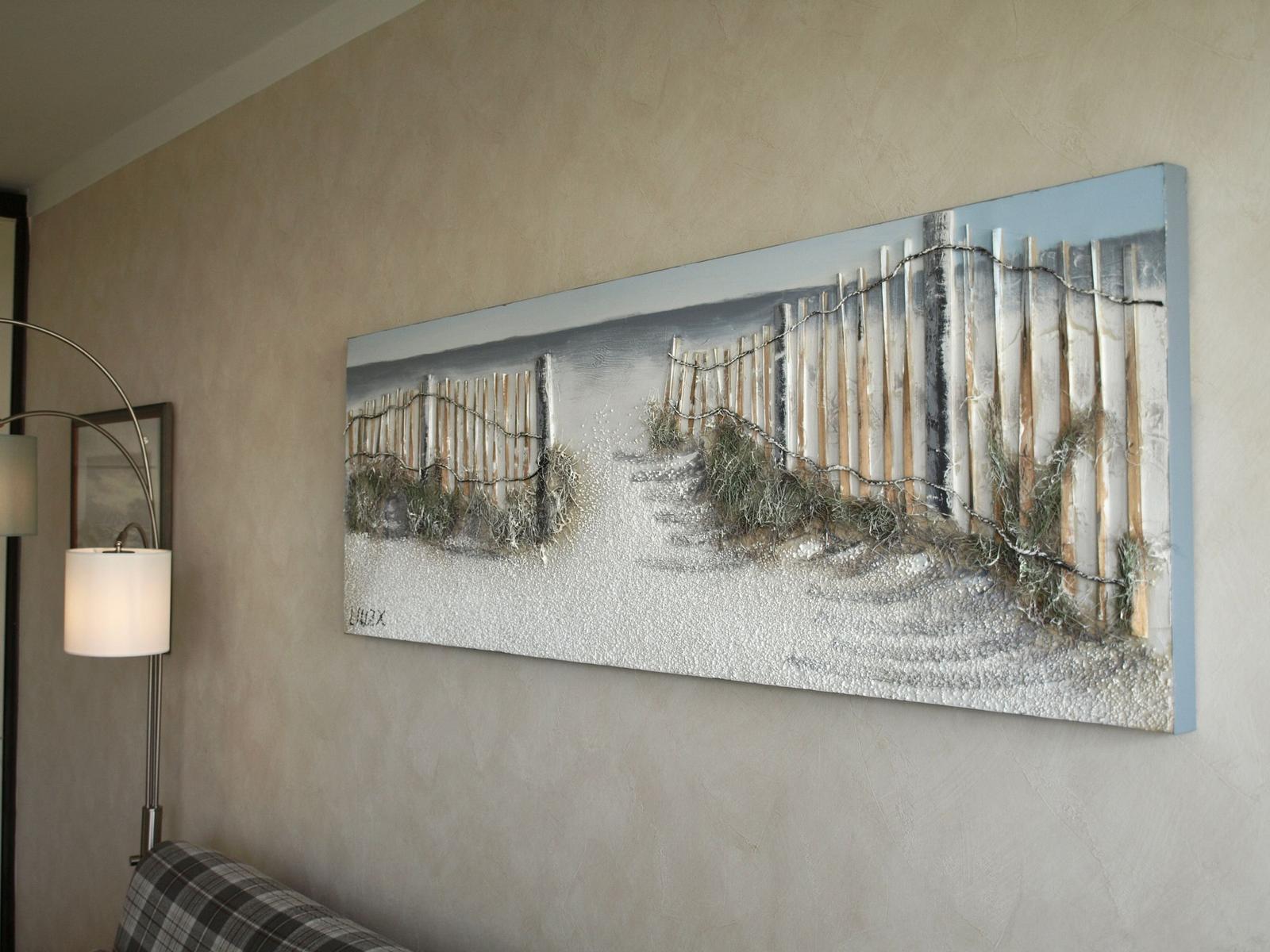 Ein Wandbild zeigt einen Strand mit Holzzaun und Gras. Links steht eine Stehlampe.