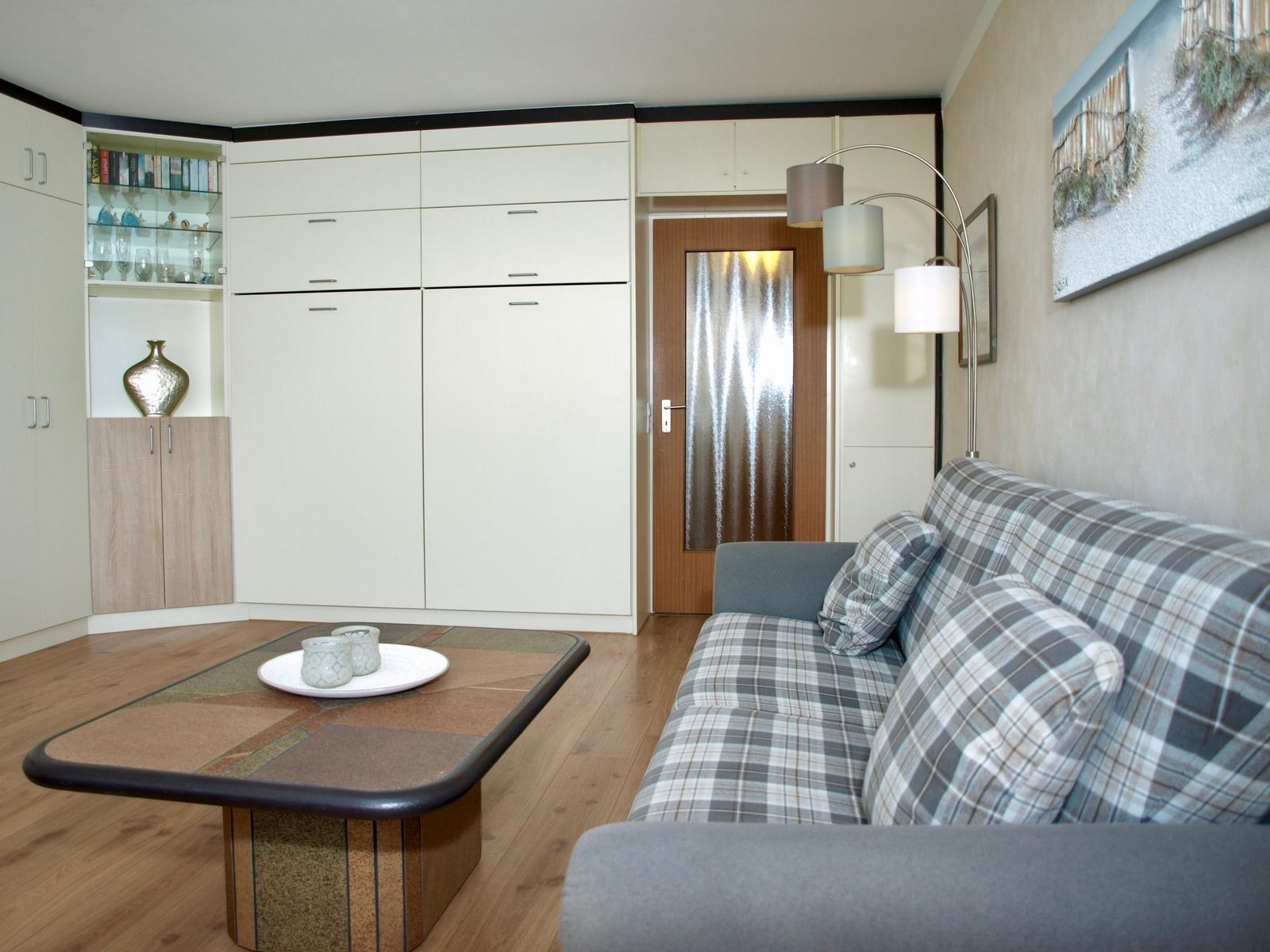 Wohnzimmer mit Sofa, Couchtisch und integrierten Schränken. Wandbild und Stehlampe sichtbar.