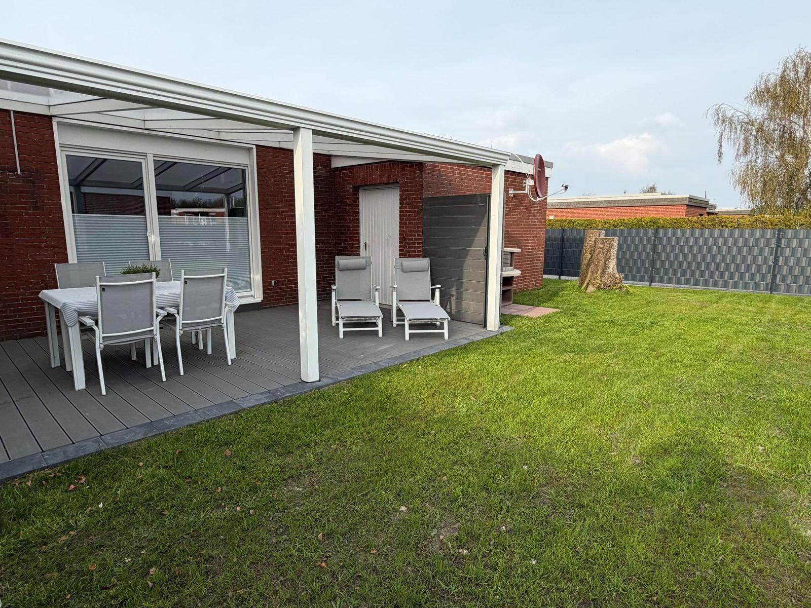 Terrace with table, chairs, and loungers. Lawn and fence in the background.