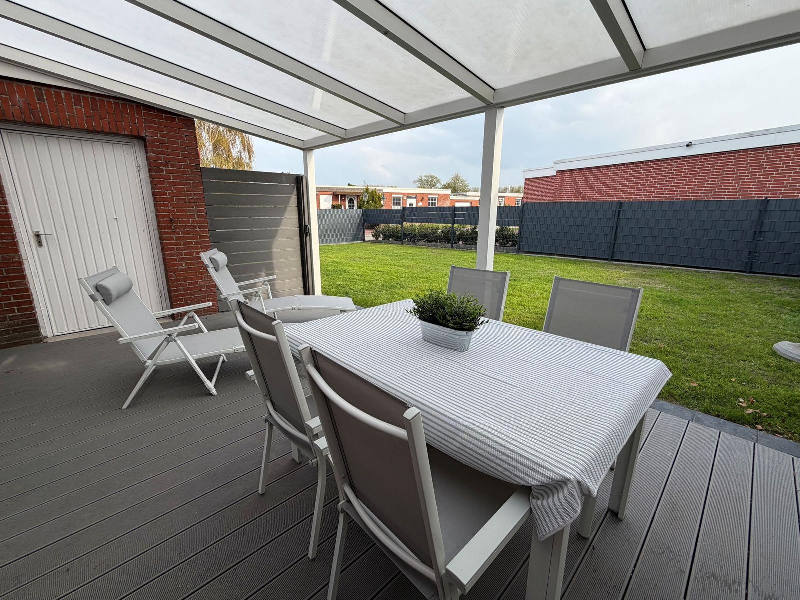 Deck with table, chairs, and awning over green lawn.