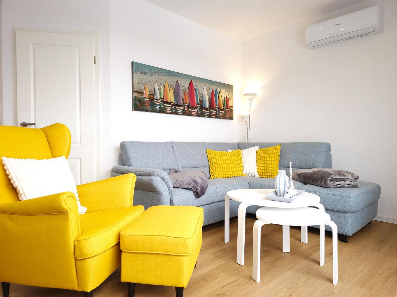 A living room with a gray sofa, yellow armchair, and wall art of sailboats.