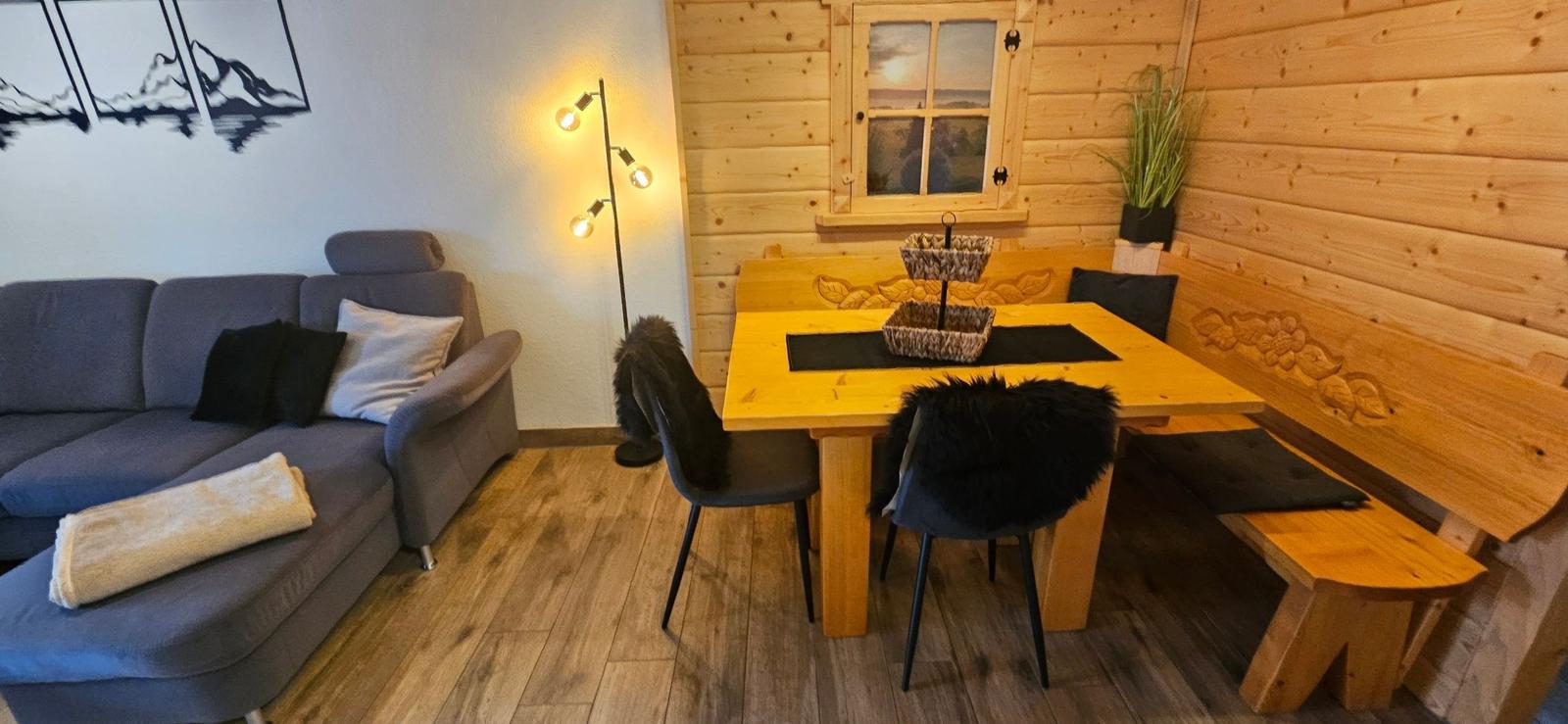 Essbereich mit Holztisch, Bänken und Stühlen. Wohnbereich mit Sofa und Wandbild.