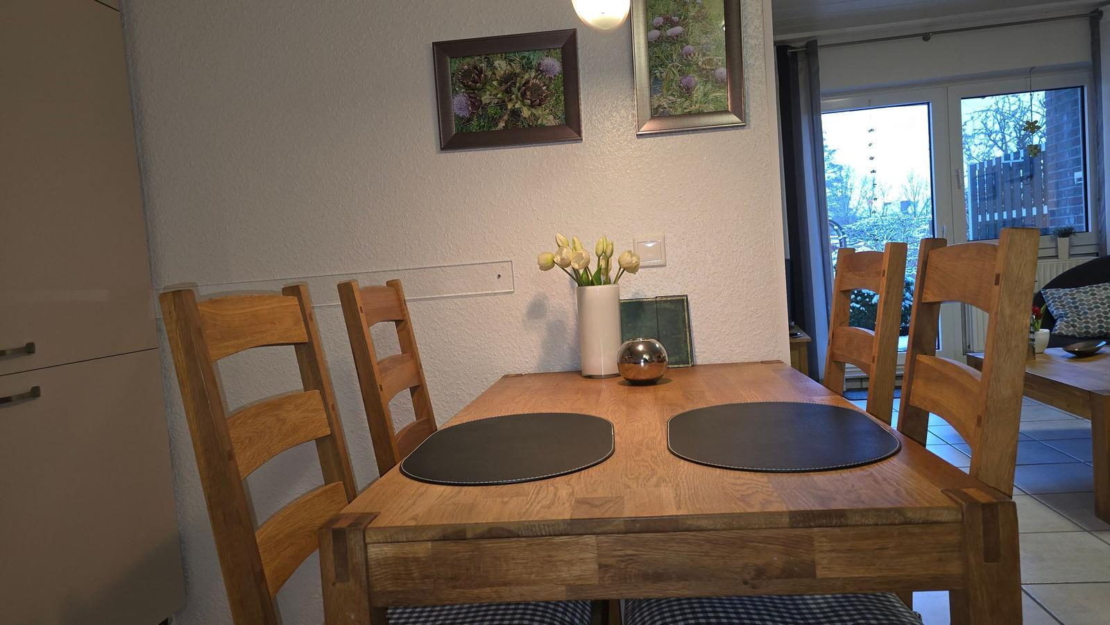 Holztisch mit vier Stühlen, Blumenvase und Bildern an der Wand.