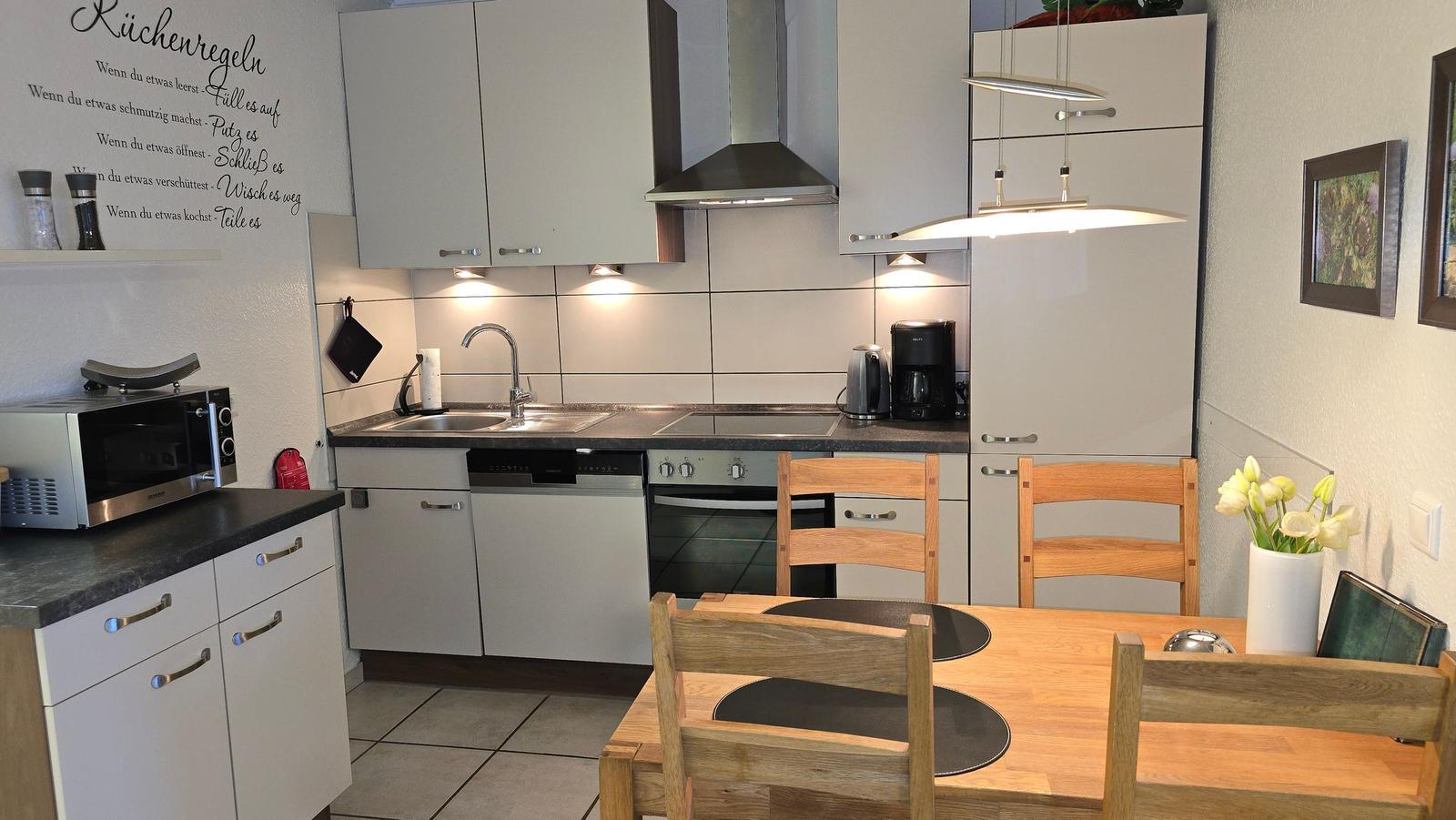 Küche mit Essbereich, Holztisch, Stühle, Kühlschrank, Herd und Spüle.