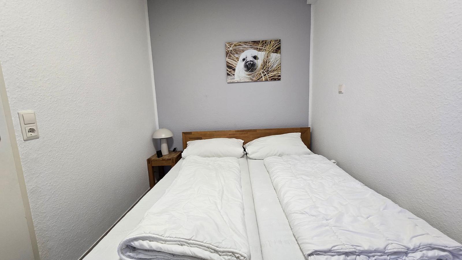 Schlafzimmer mit Doppelbett, Nachttisch und Wandbild eines Seehundes.