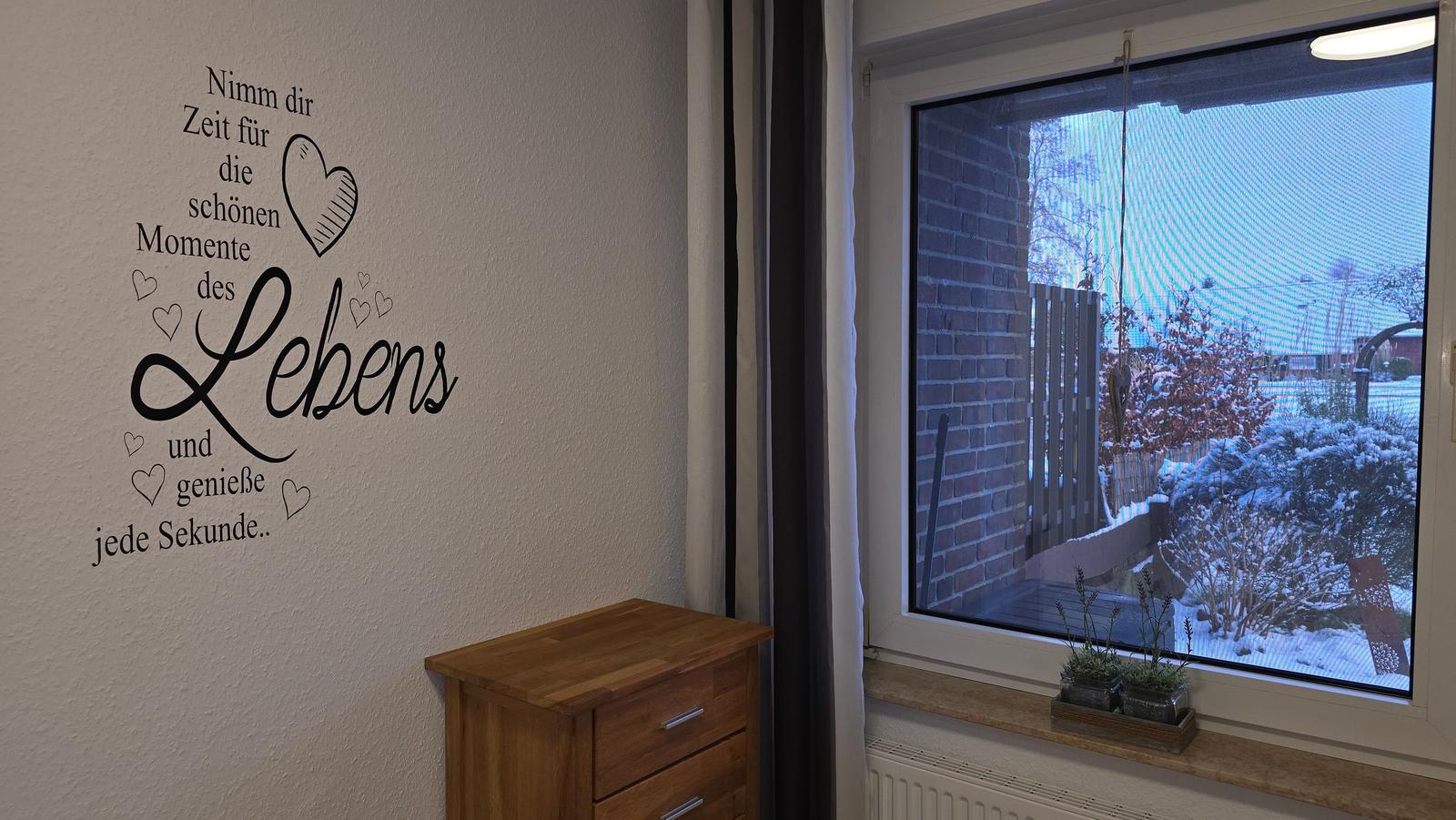 Wand mit Aufkleber: Nimm dir Zeit für die schönen Momente des Lebens. Fenster mit Blick auf Schnee.