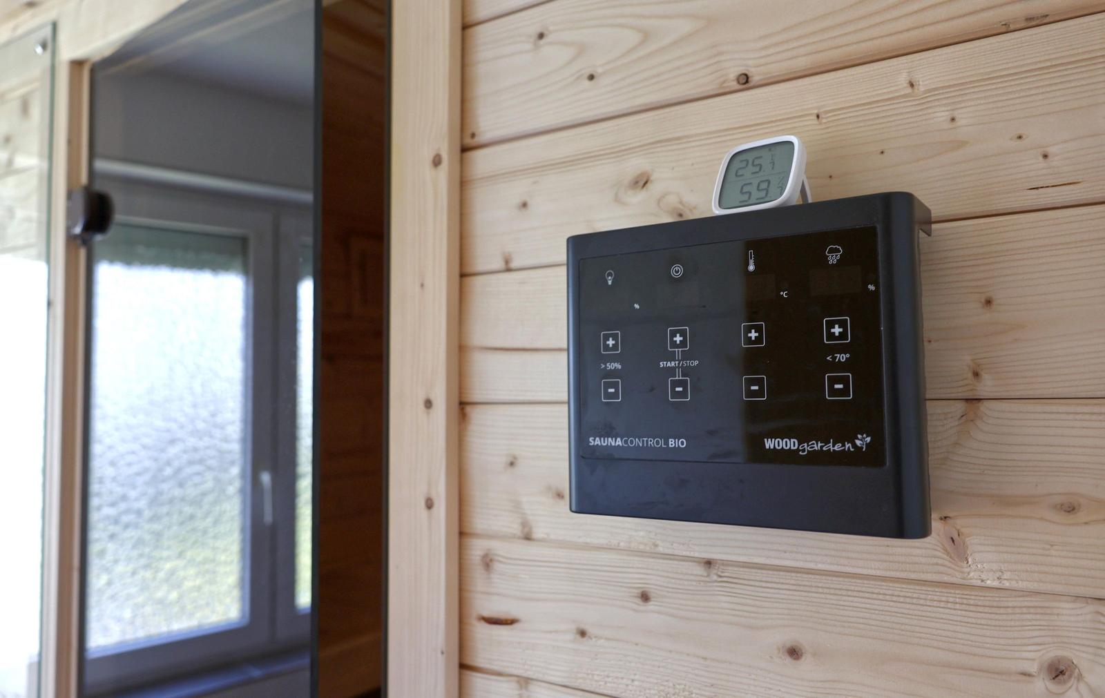 Sauna-Kontrollgerät an Holzwand mit Temperaturanzeige und Fenster im Hintergrund.