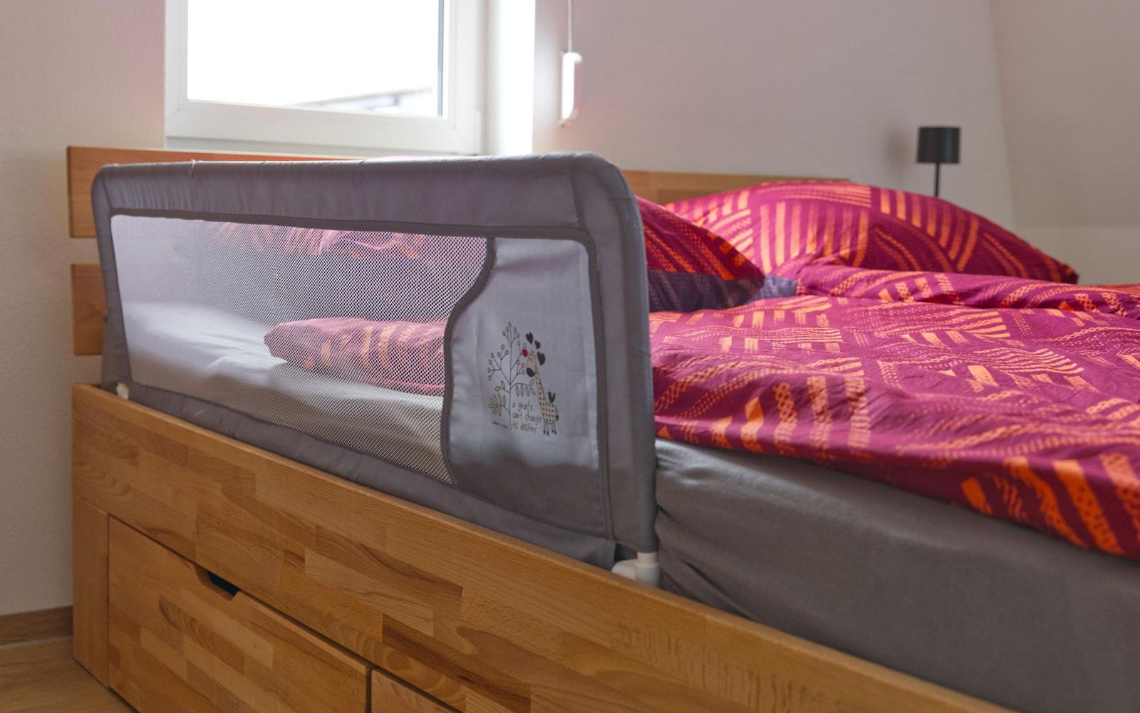 Ein Bett mit Holzrahmen und einem Babygitter an der Seite.